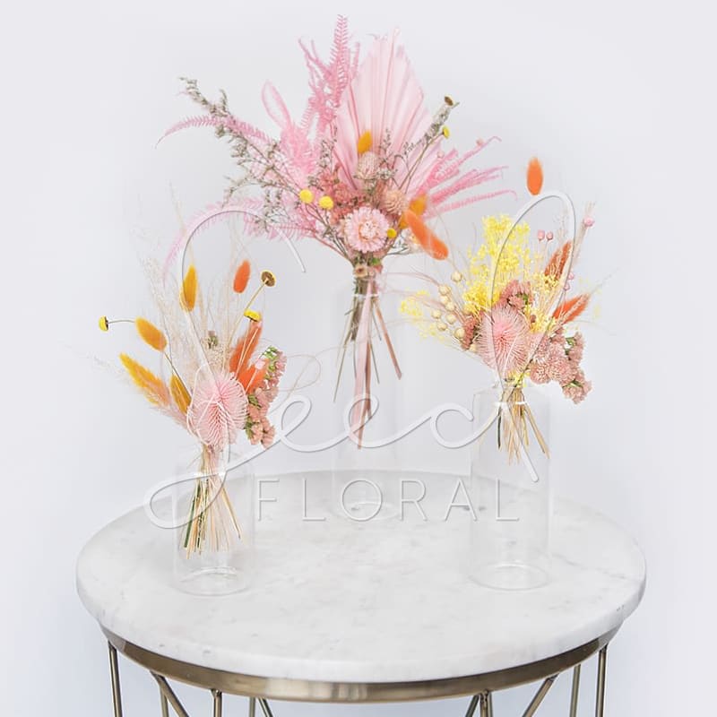 Three pastel dried-flower bouquets in clear glass vases on a round table.