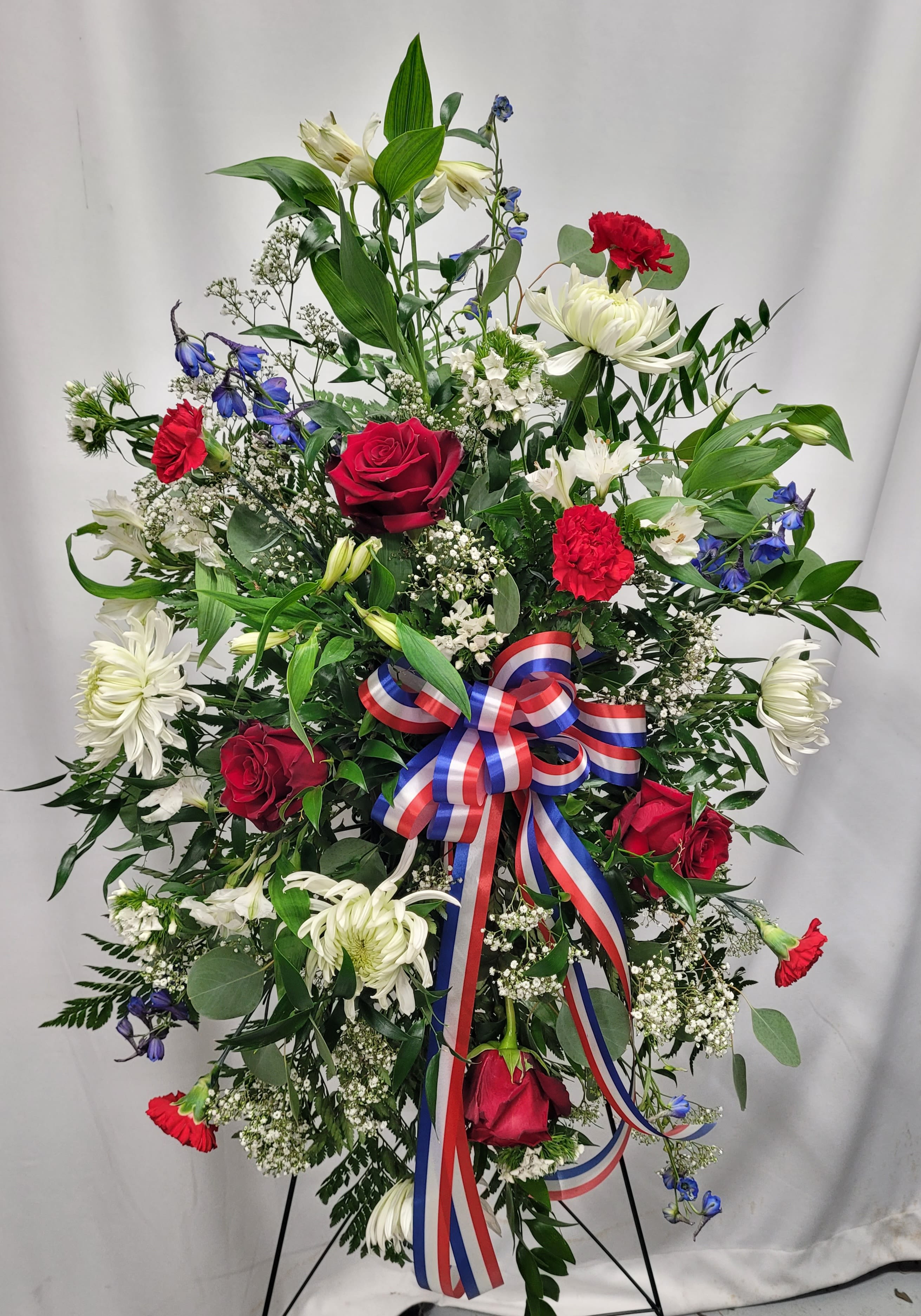 Standing floral spray with red roses, white lilies, and a red-white-blue ribbon