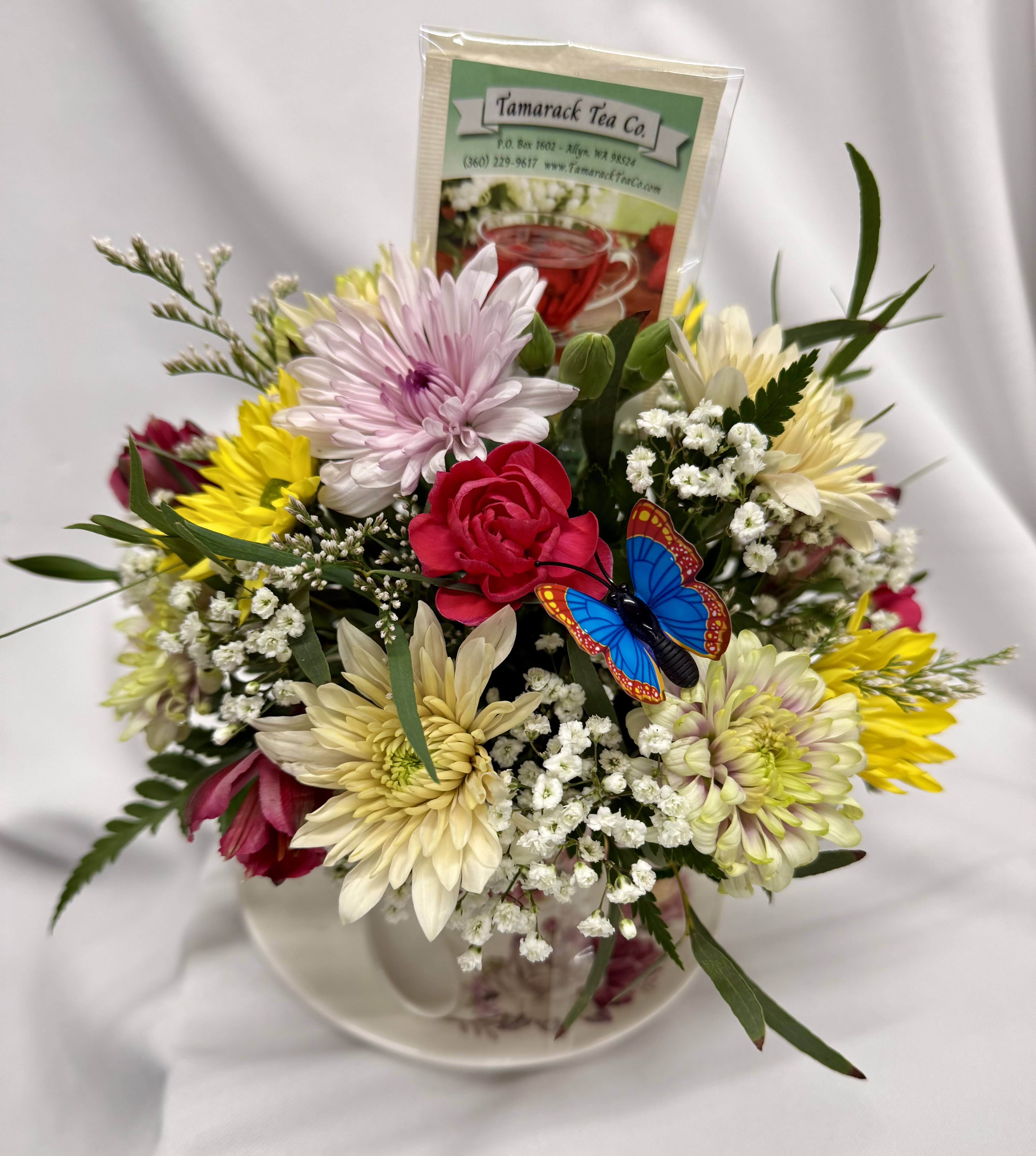 Tea party! - A cozy cluster of mixed roses, daisies, alstroemeria and chrysanthemums arranged in a low, rounded ceramic teacup and saucer makes a sweet birthday bouquet or Mother's Day gift that feels like a warm invitation to pause. This tea party flower arrangement with included Tamarack Tea Co. packets is also perfect for Get Well wishes, Thank You gestures, graduations, or a just-because surprise-the recipient will feel comforted and truly seen by the thoughtful pairing of fresh blooms and a cup of tea.  Flowers are arranged compactly to fill the floral-patterned teacup and matching saucer, with a ceramic spoon. The low profile makes it an easy bedside or desk accent; delicate filler blooms and unopened lily buds add soft texture while a few individually wrapped tea packets rise gently from the back to add color and a small consumable gift.  Choose to have us select an assortment of Tamarack Tea Co. flavors or specify your preference in the special instructions-available caffeinated options include Sir Earl Grey, Black Elderberry, and Chai. Decaf &amp; herbal choices include Starfruit Kiwi, Bourbon Street Vanilla, Chocolate Mint Rooibos, Angel Mist, Blue Mango, Amazing Apricot Honey, and Kyoto Cherry. This keepsake teacup arrangement arrives ready to brighten a spring or summer with warmth and charm.