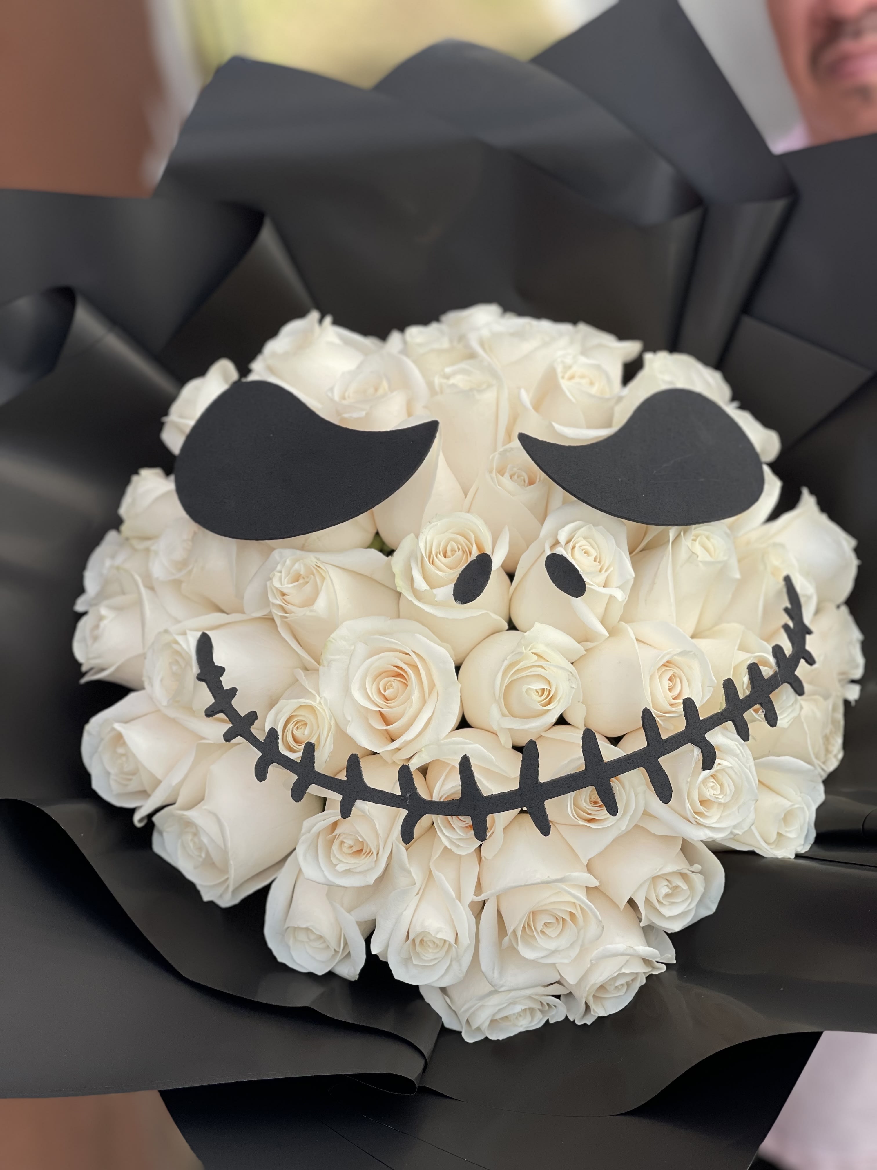 White rose bouquet wrapped in black paper with a skull face design