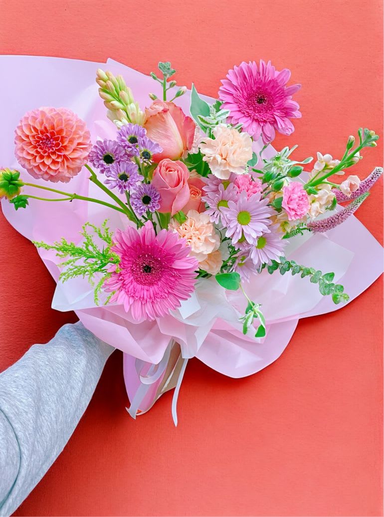 Hand-tied bouquet of pink and lavender flowers wrapped in pale paper