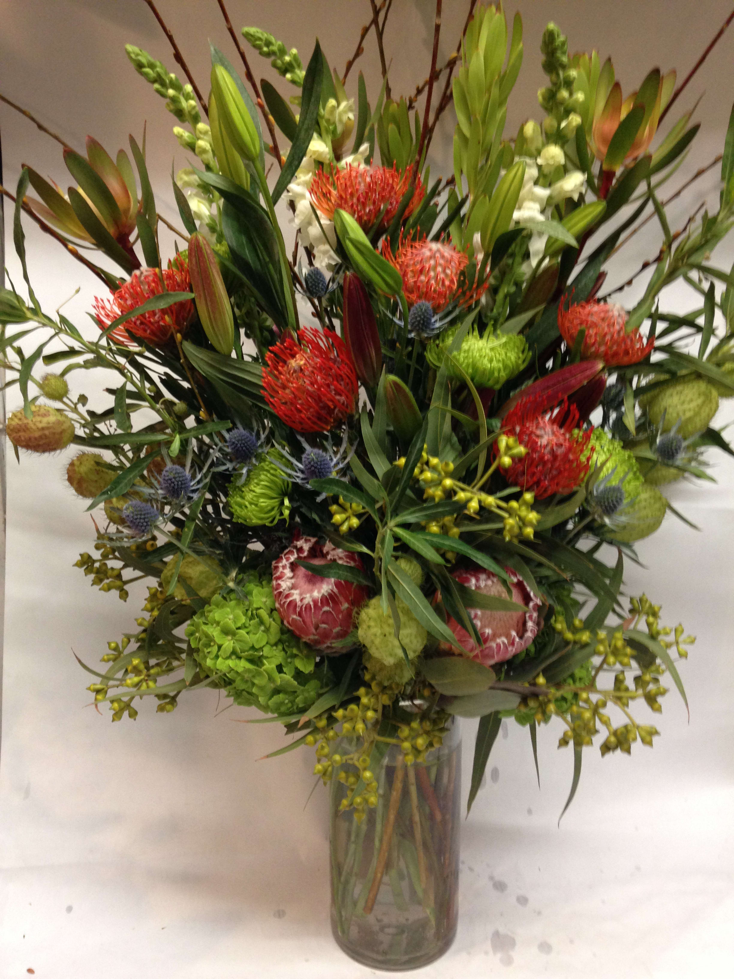 Tall mixed bouquet in a glass vase with red and green blooms
