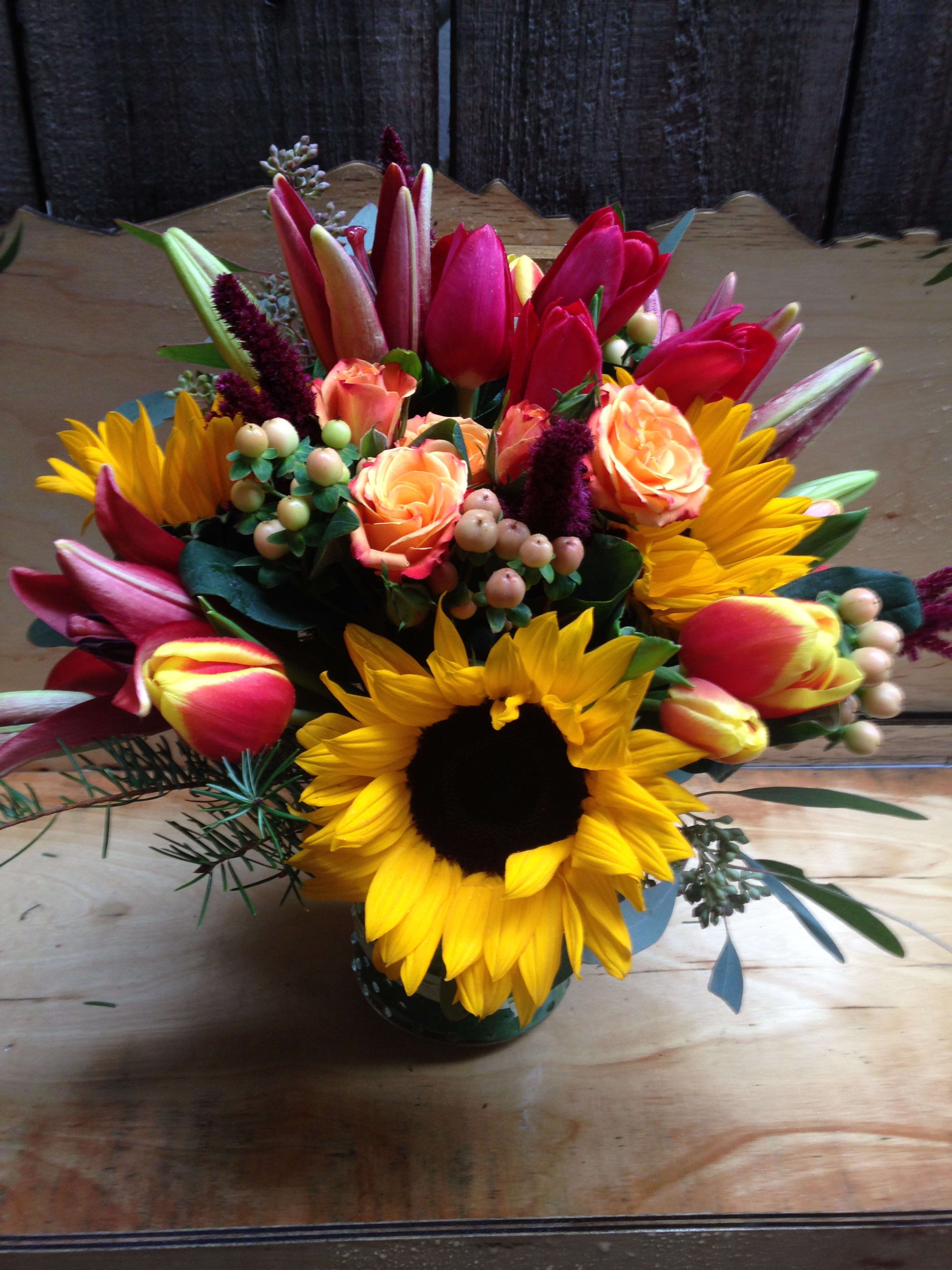 Bright mixed bouquet with sunflowers, tulips, and peach roses in a vase