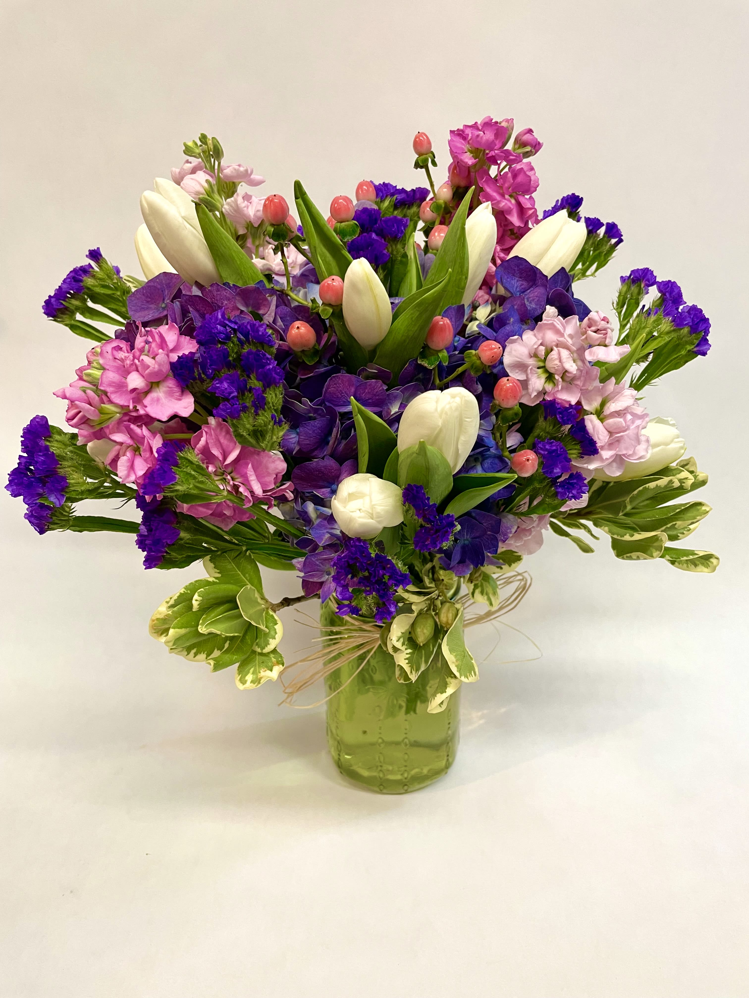 Colorful bouquet of tulips, purple blooms, and pink flowers in a green glass vase