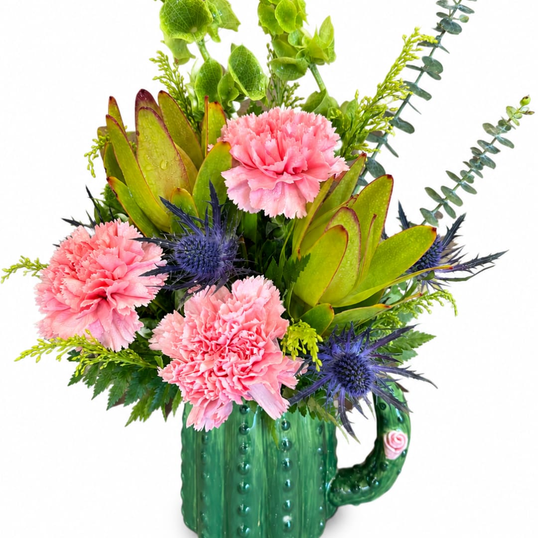Pink carnations and blue thistles arranged in a green ceramic mug