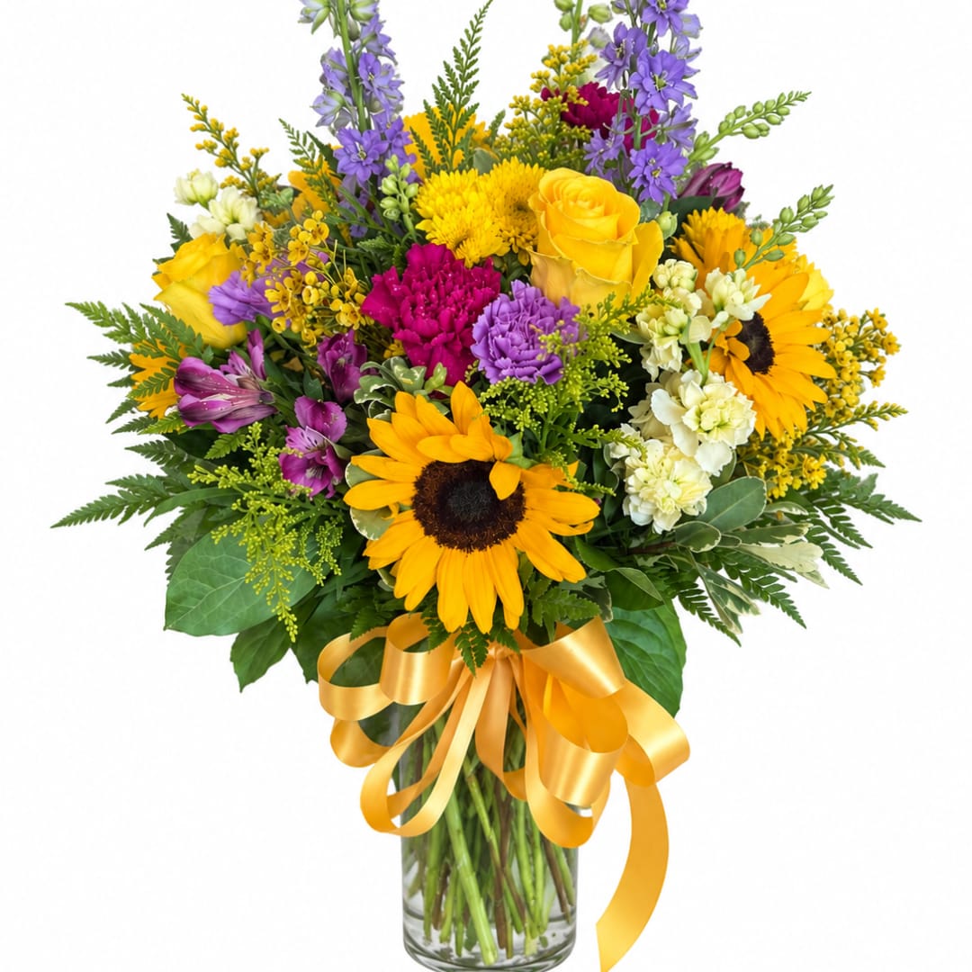 Mixed bouquet of sunflowers, roses, and purple flowers in a glass vase with a yellow ribbon