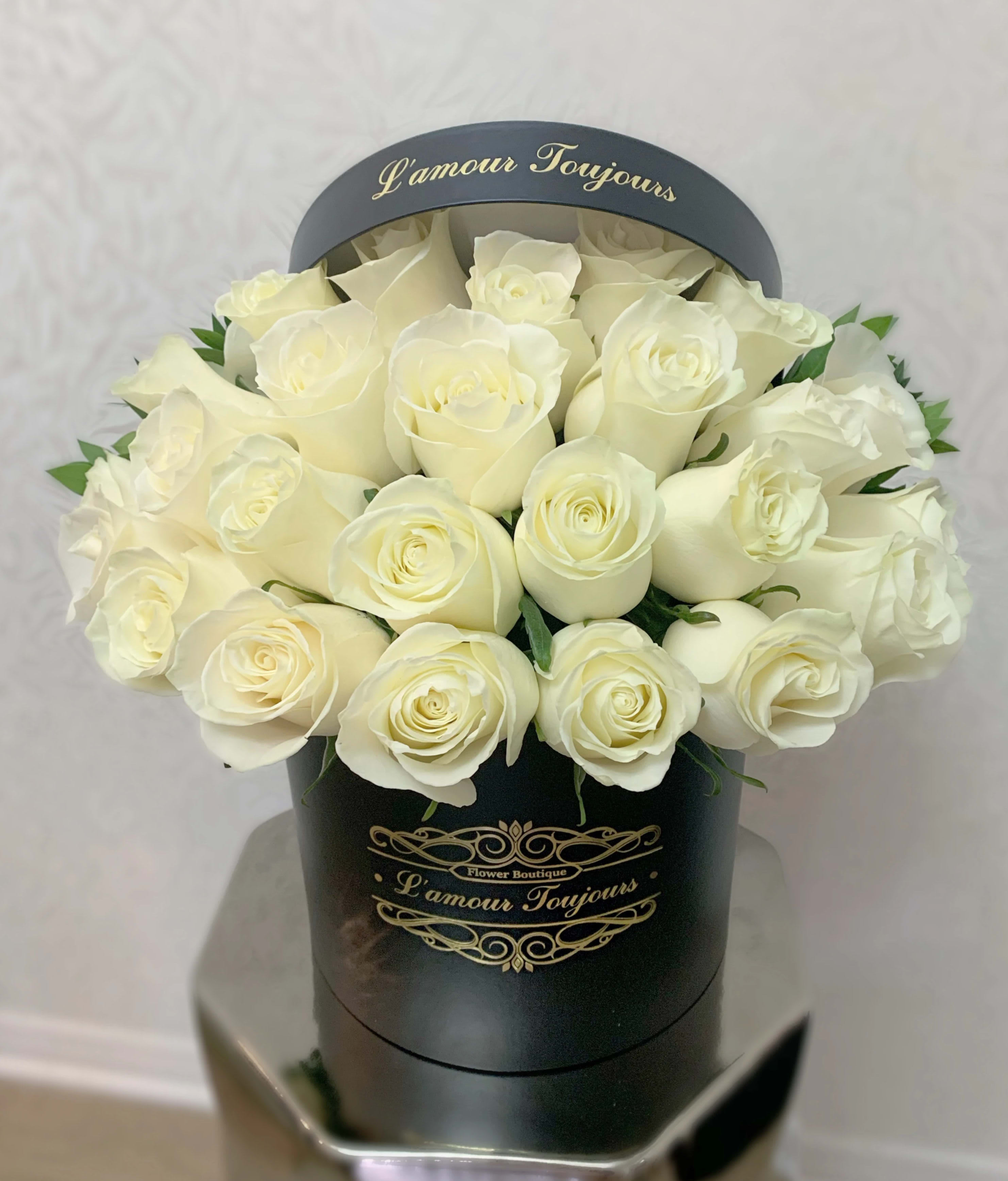 White roses arranged in a black round box with gold lettering