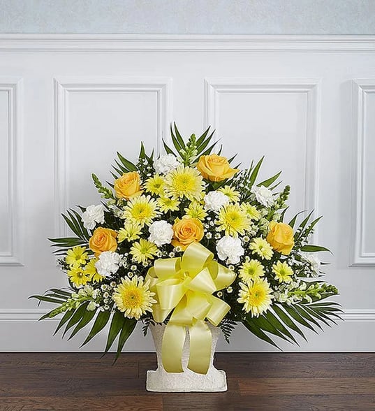 Yellow and white floral arrangement in a white vase with a yellow ribbon