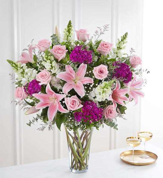 Pink lilies and roses arranged in a clear glass vase