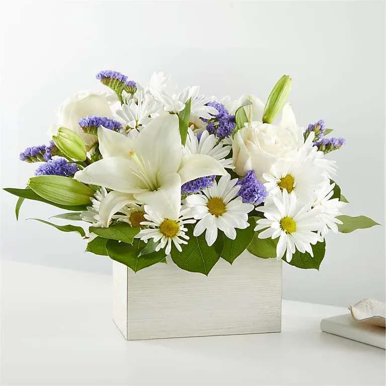 White lilies and daisies arranged in a square white box with purple accents