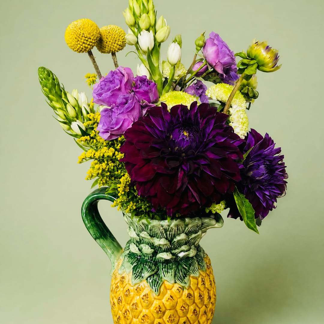 Purple and white flowers arranged in a pineapple-shaped ceramic pitcher
