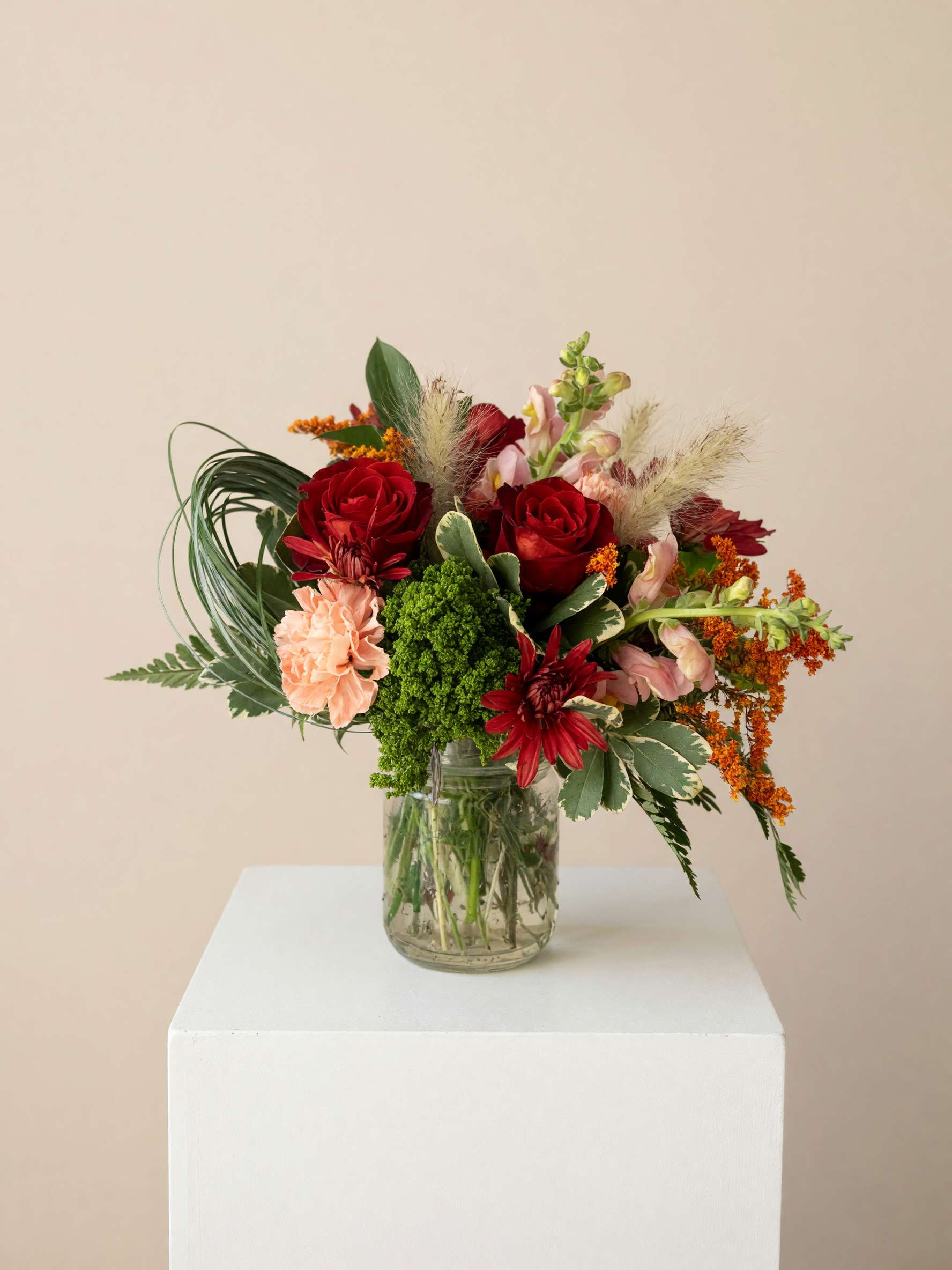 Mixed bouquet of red, pink, and orange flowers in a glass jar vase