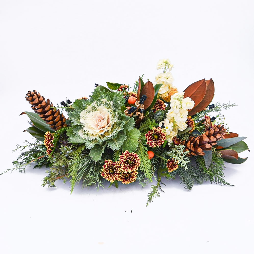 Low centerpiece with ornamental cabbage, mums, white flowers, evergreens, and pinecones.