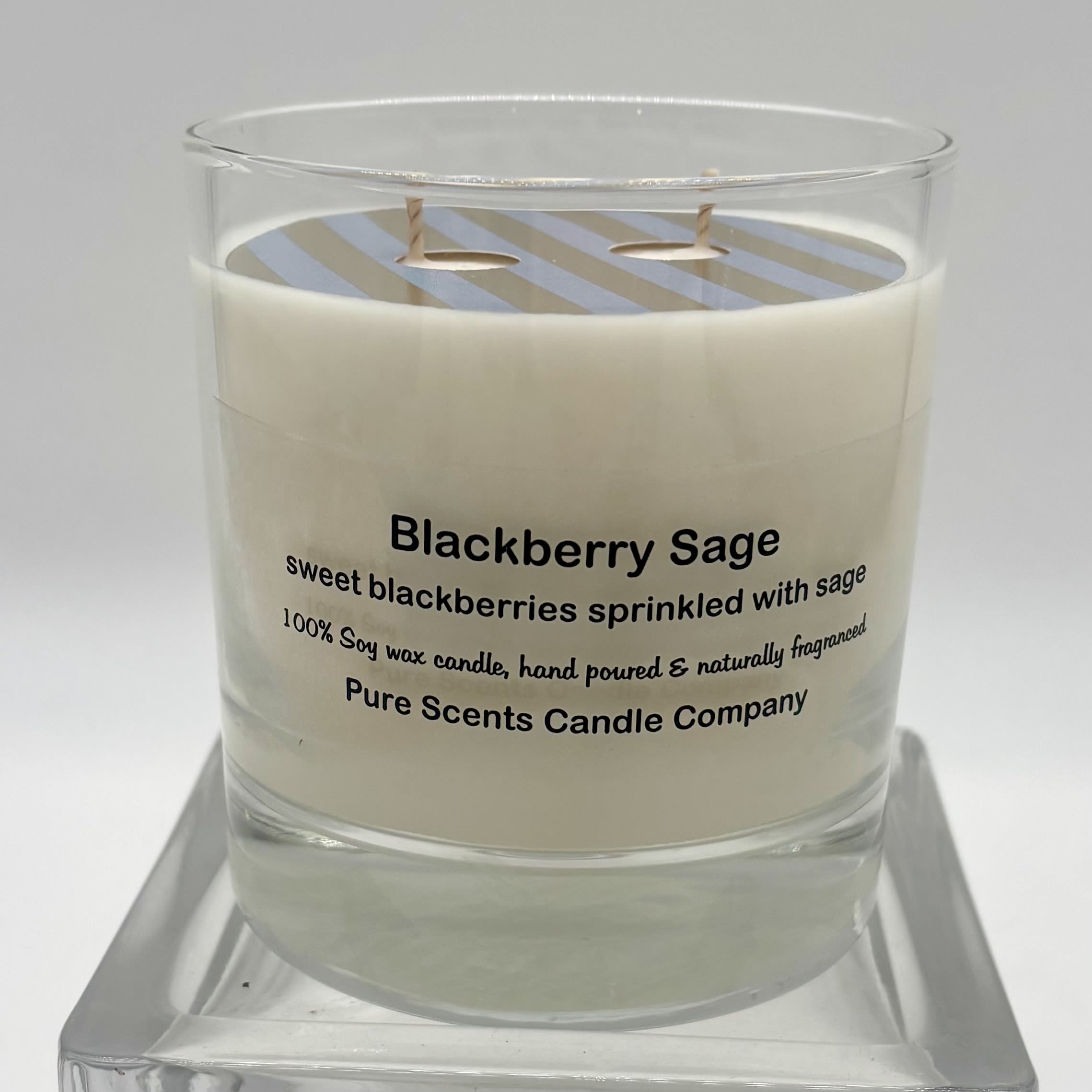 White Blackberry Sage scented candle in a clear glass jar on a glass stand