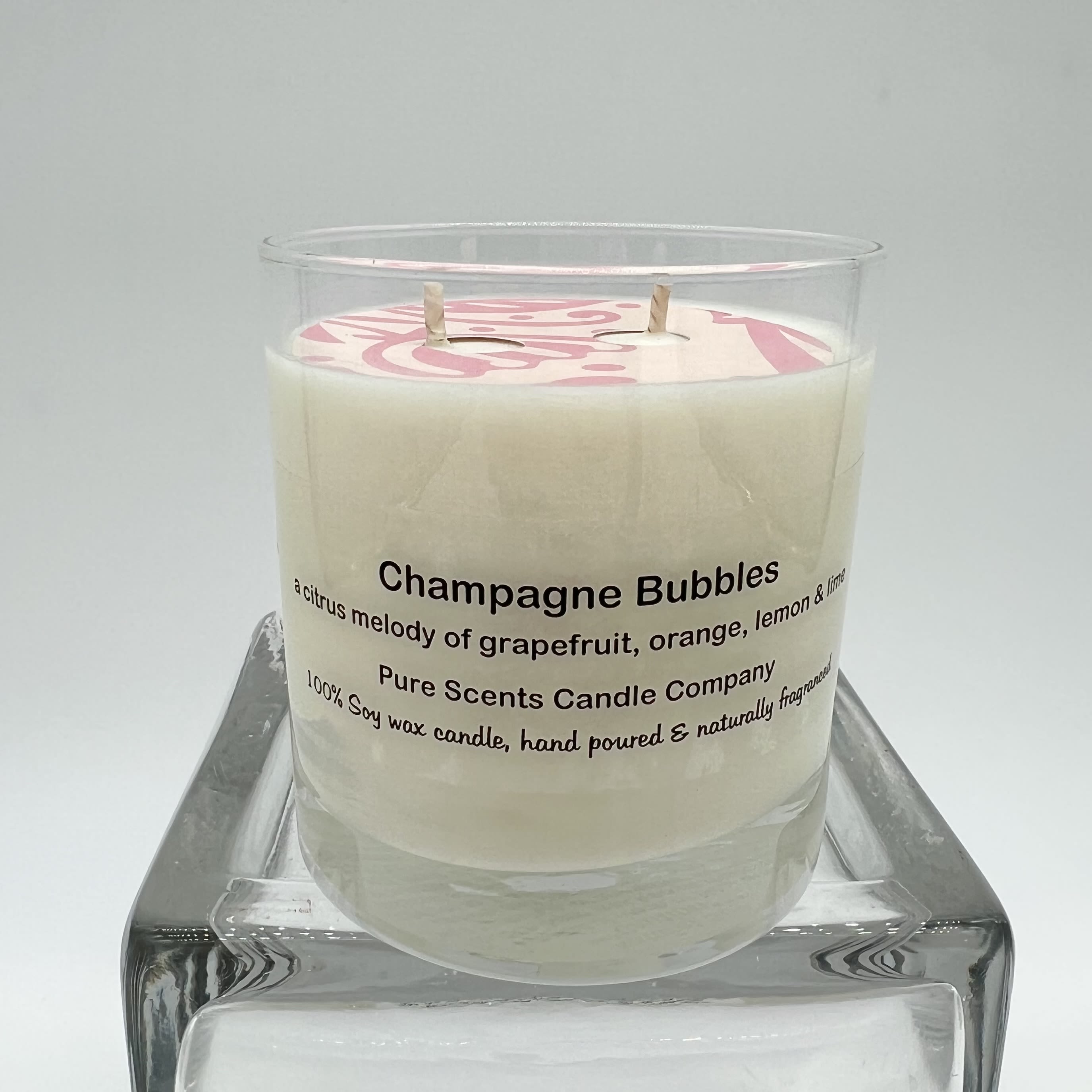 White soy wax candle labeled Champagne Bubbles in a clear glass jar on a glass stand