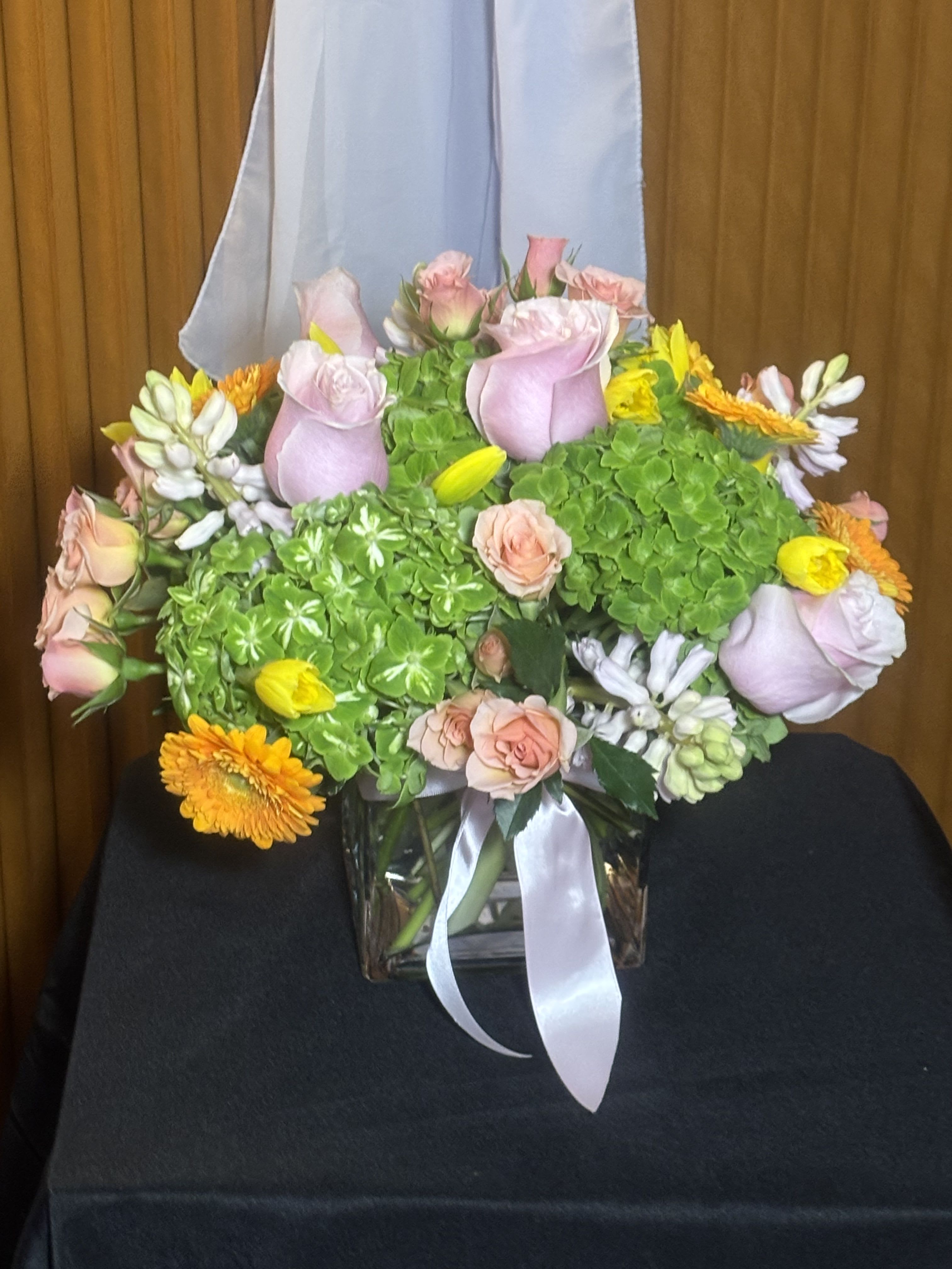 Pink roses and yellow-orange flowers in a glass vase with a white ribbon