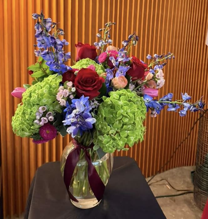 Bouquet of red roses, green hydrangeas, and blue flowers in a glass vase