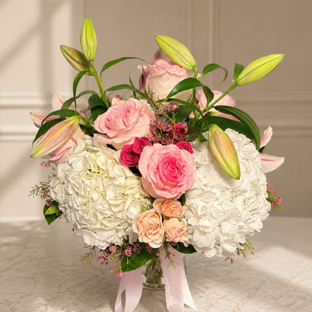 Pink roses and white hydrangeas in a glass vase with lily buds