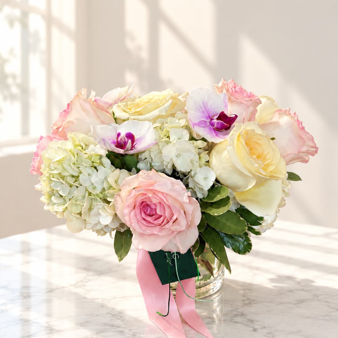 Pink and cream roses with white hydrangeas and orchids in a glass vase