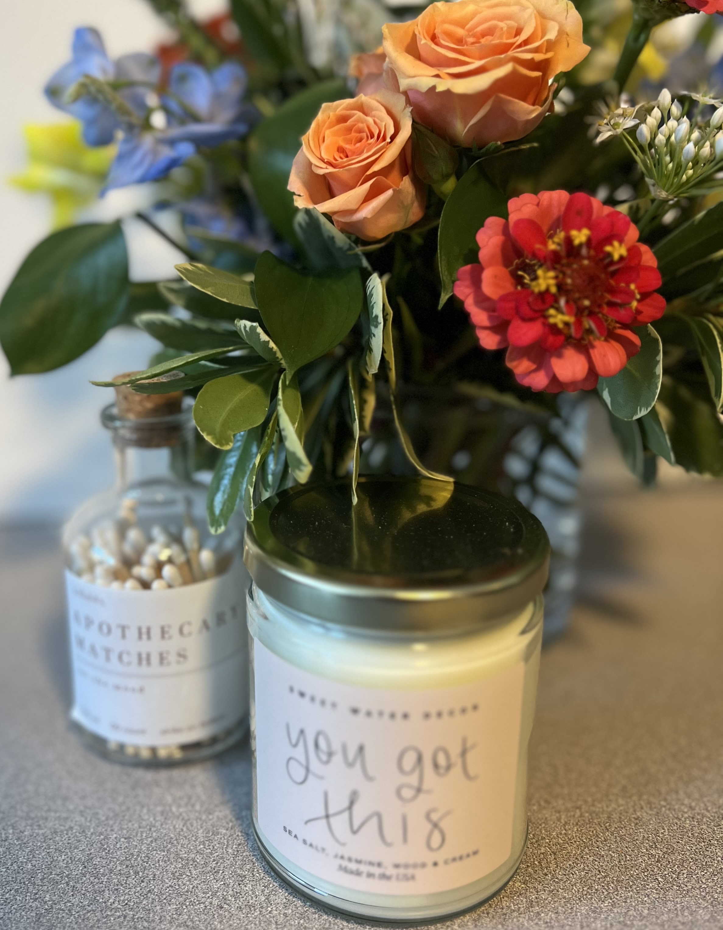 Small floral arrangement in a glass jar with roses and a red zinnia, beside candles