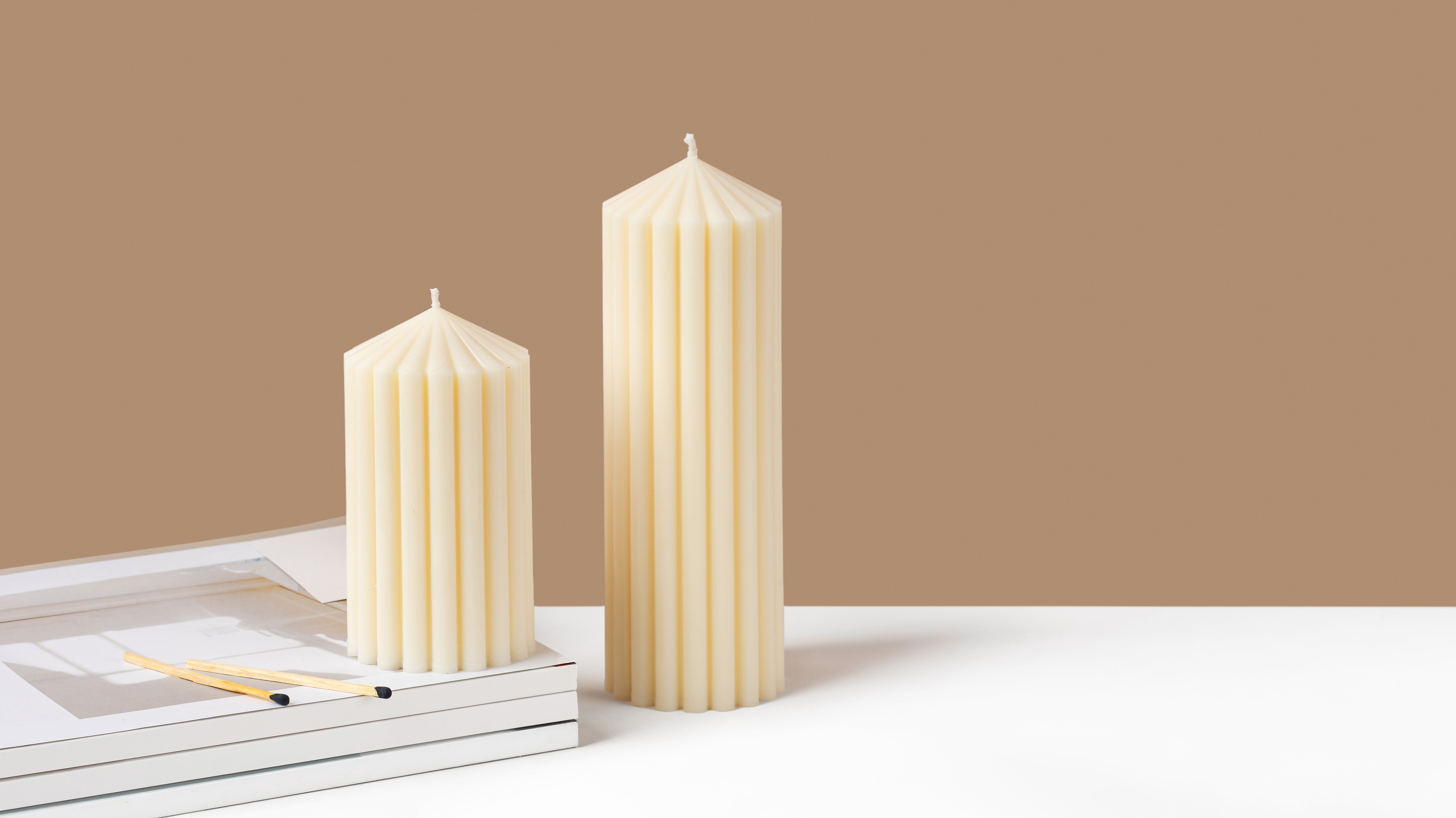 Two cream pillar candles on a white surface with matches nearby