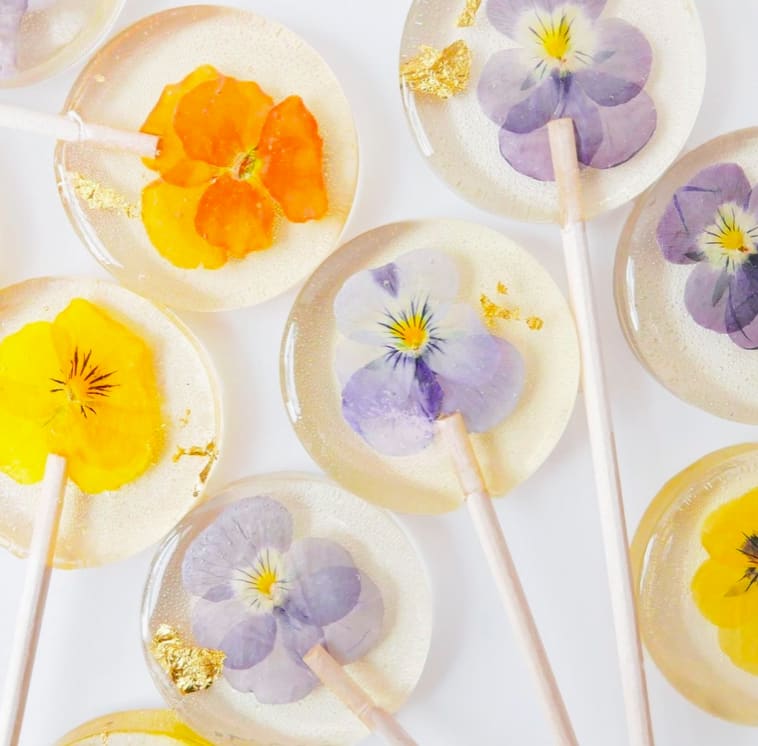 Clear lollipops with pressed yellow and lavender flowers and gold leaf on a white background