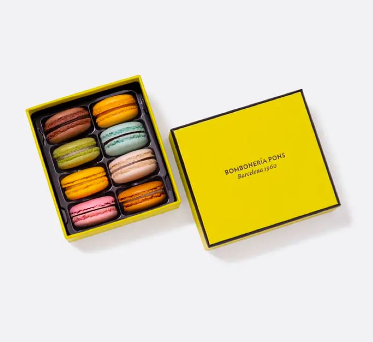 Box of colorful macarons with a yellow lid beside it