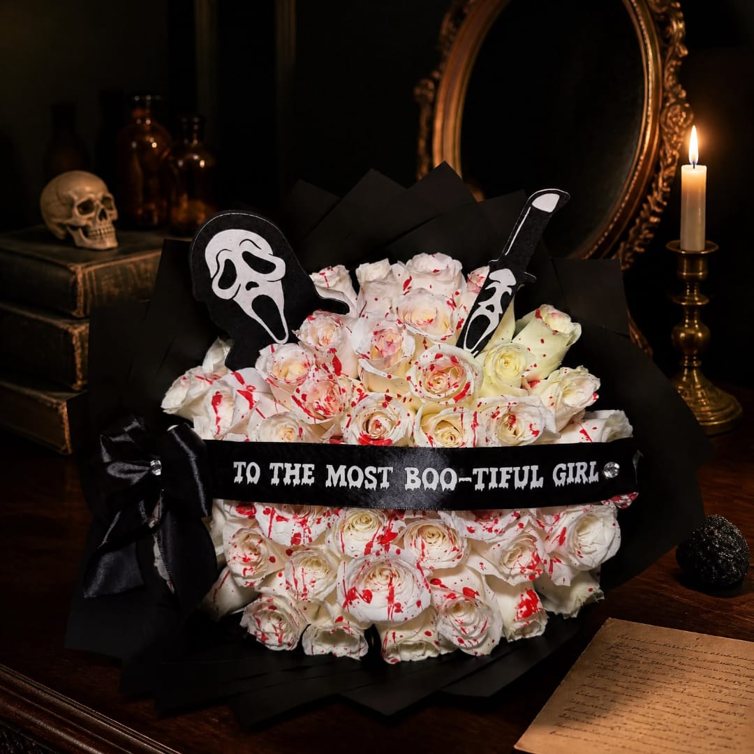 White roses with red splatter accents in black wrap and Halloween picks