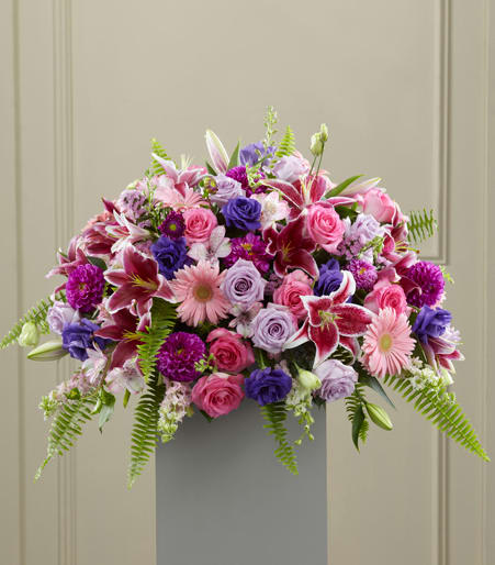 Large pink and purple flower arrangement with lilies, roses, and gerbera daisies on a gray pedestal stand
