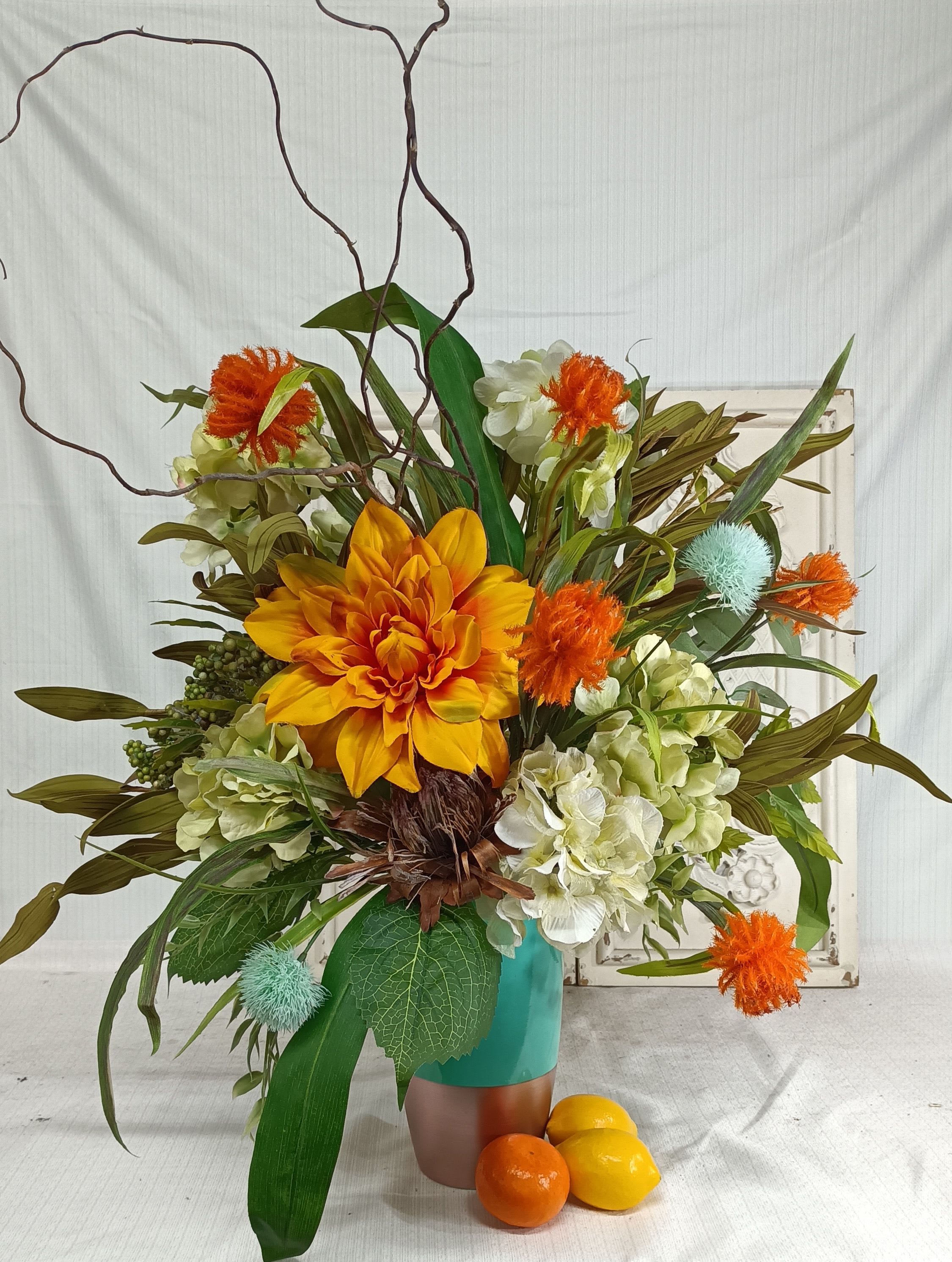 Orange and white floral arrangement in a turquoise vase with decorative branches