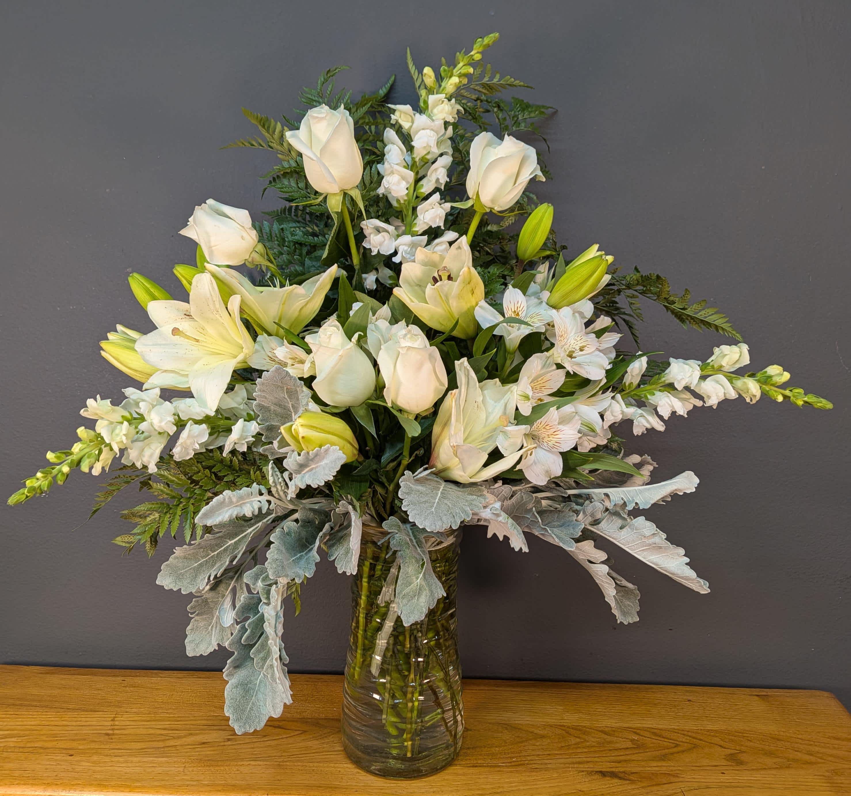 White lilies and roses arranged in a glass vase with silver foliage