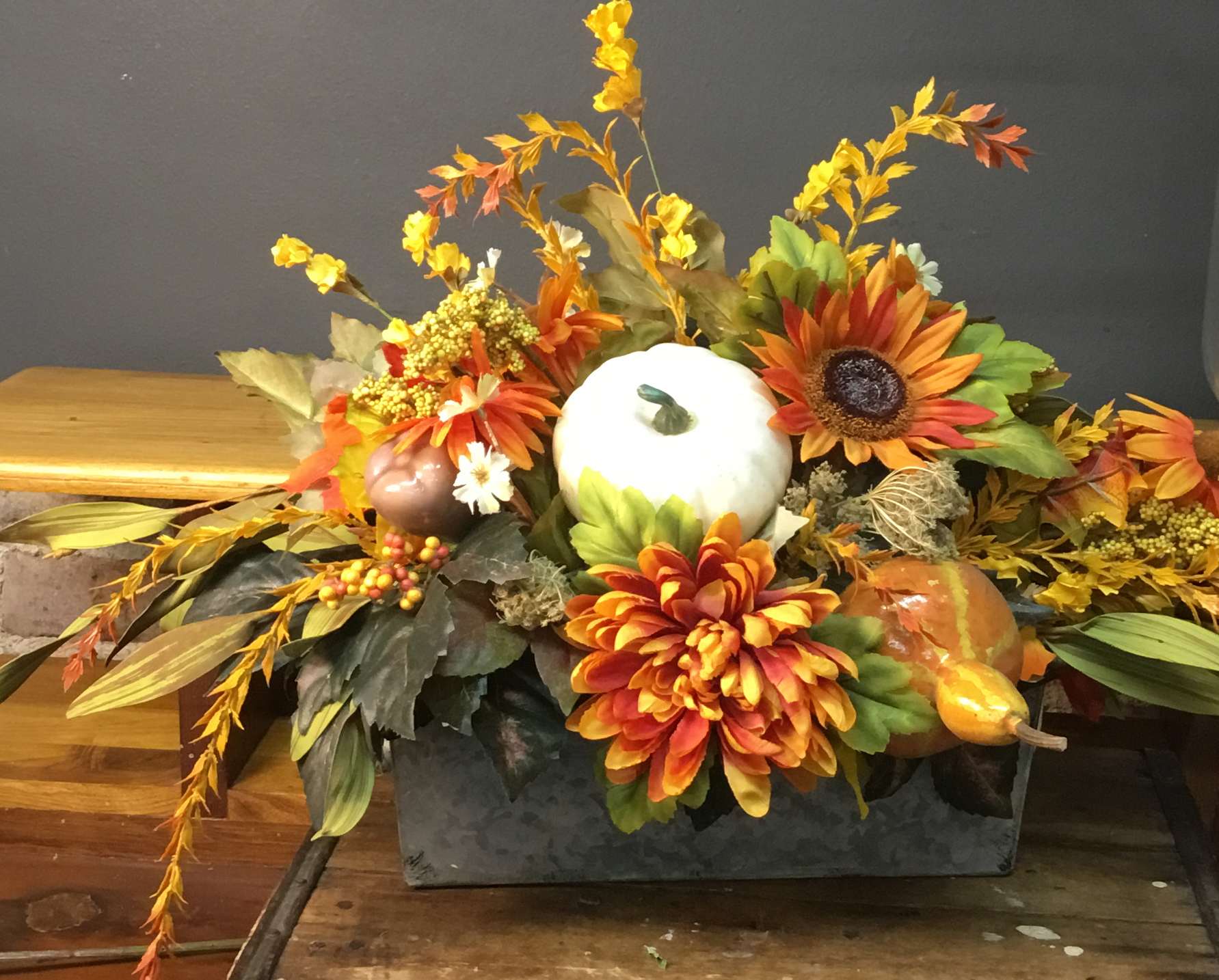 Autumn centerpiece with orange flowers, pumpkins, and a white gourd in a rectangular container