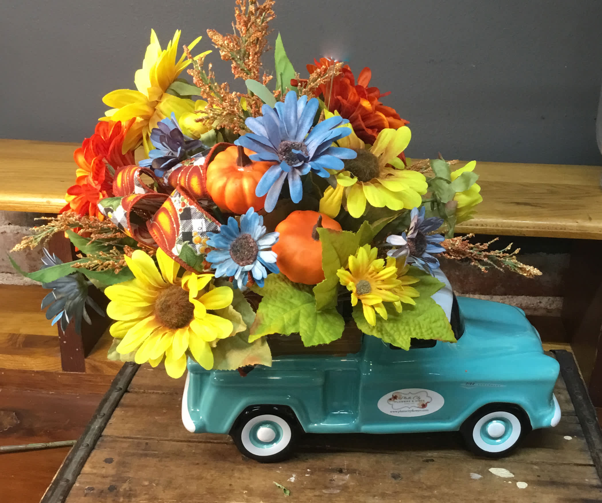 Fall floral arrangement in a turquoise truck-shaped container with pumpkins