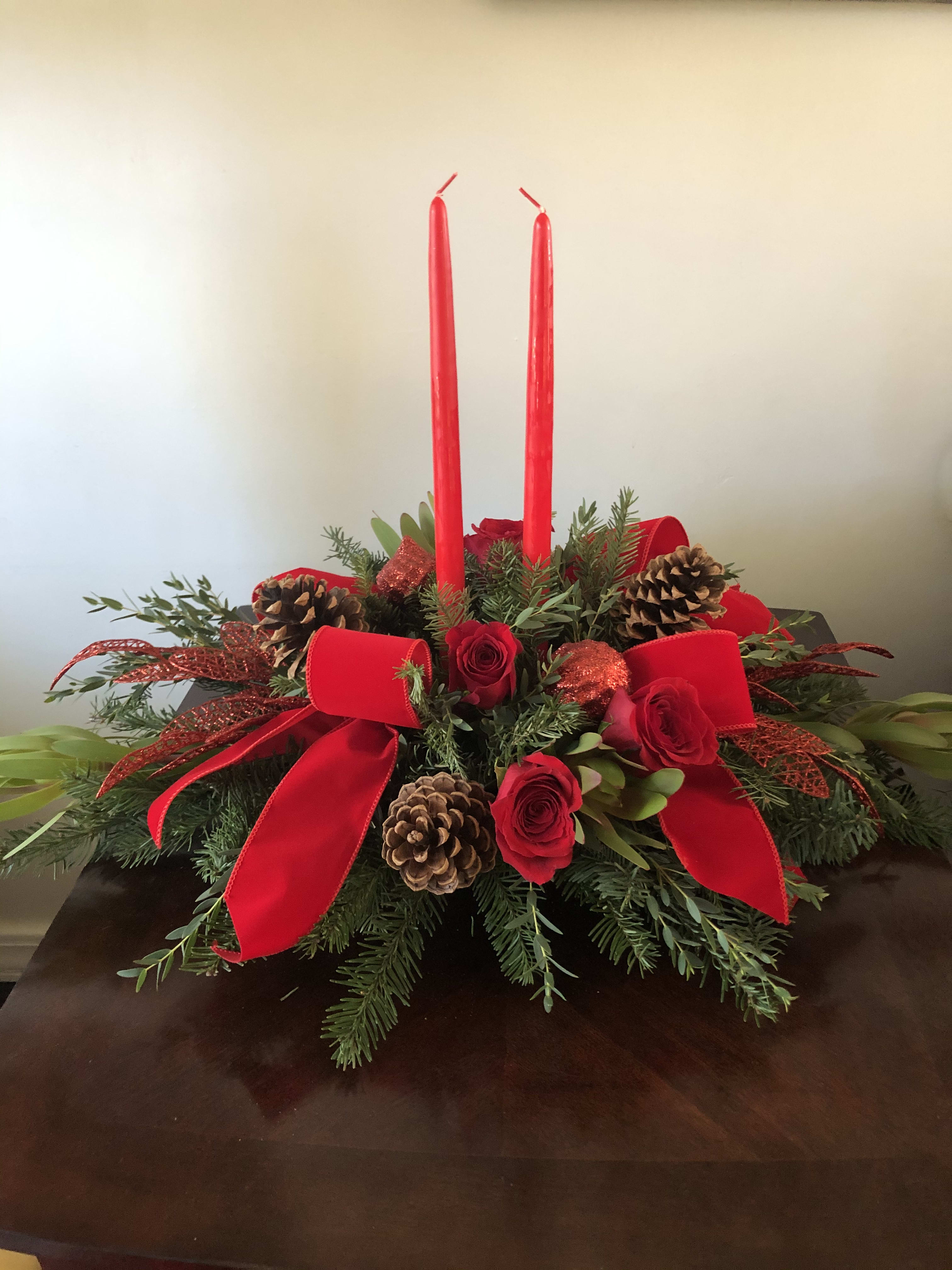 Red roses and candles arranged with pinecones and ribbon