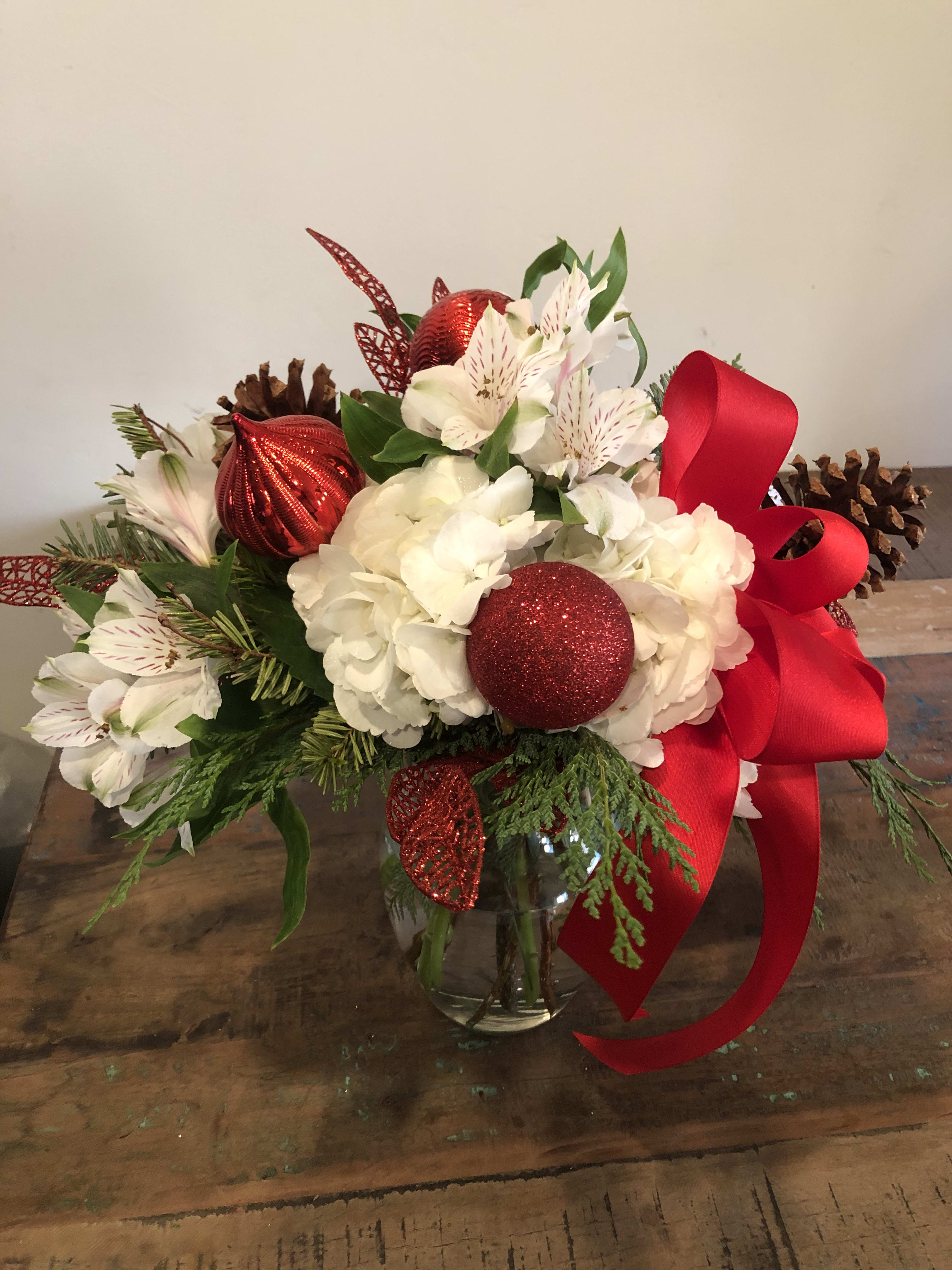 Holiday bouquet of white flowers with red ornaments and ribbon in a glass vase