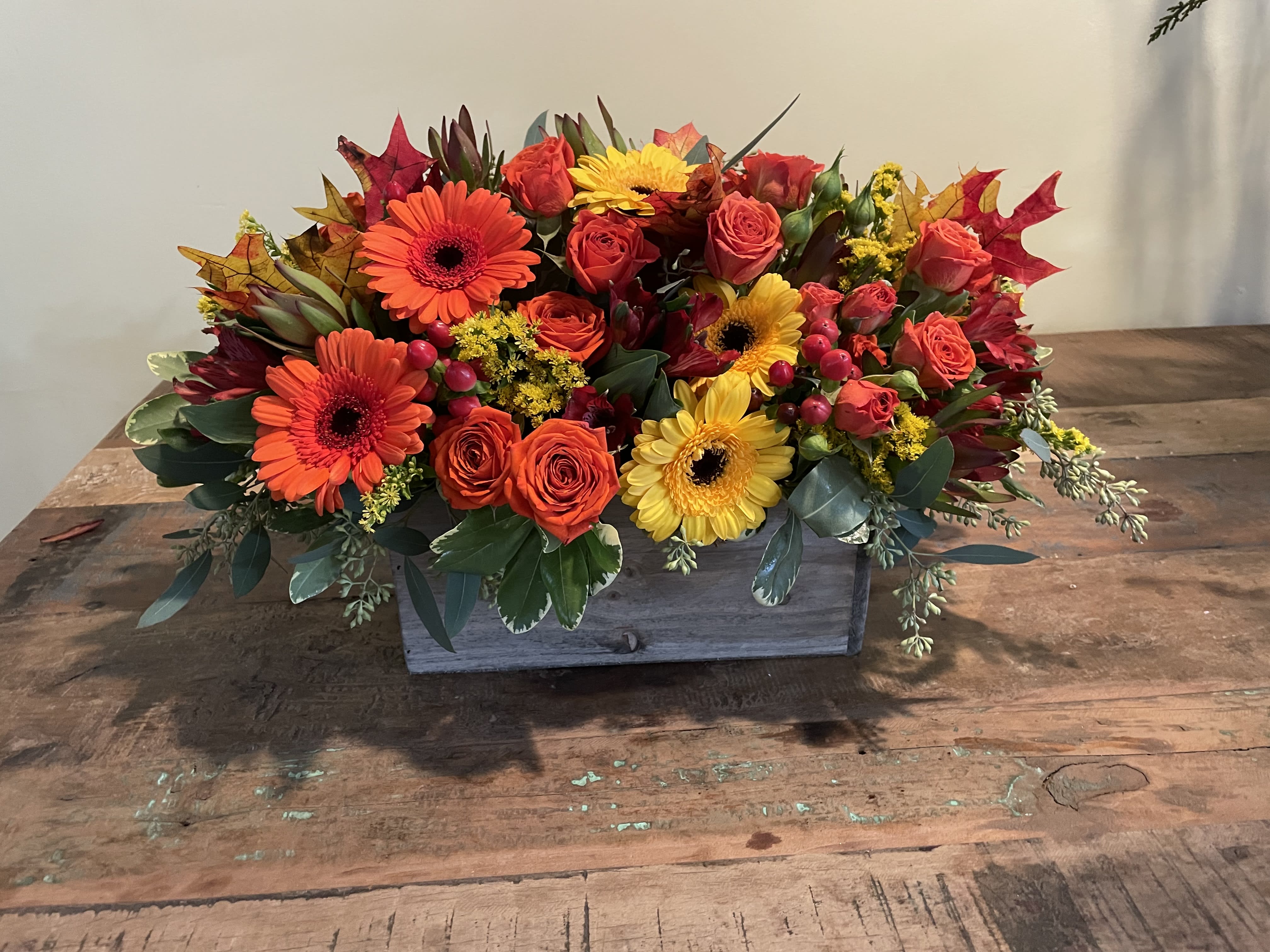 Rectangular floral arrangement with orange, yellow, and red blooms in a wooden box