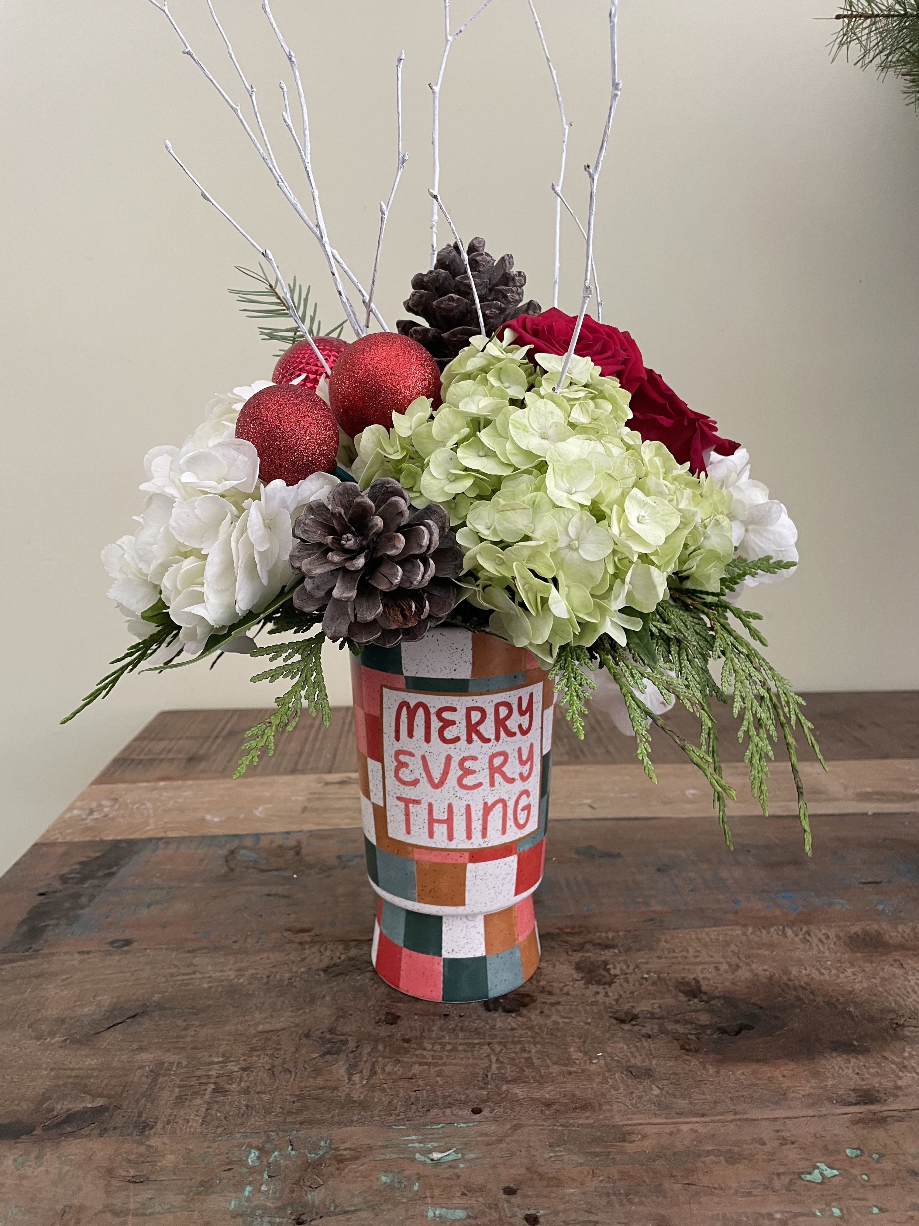 Holiday floral arrangement in a patterned vase with red ornaments and pinecones