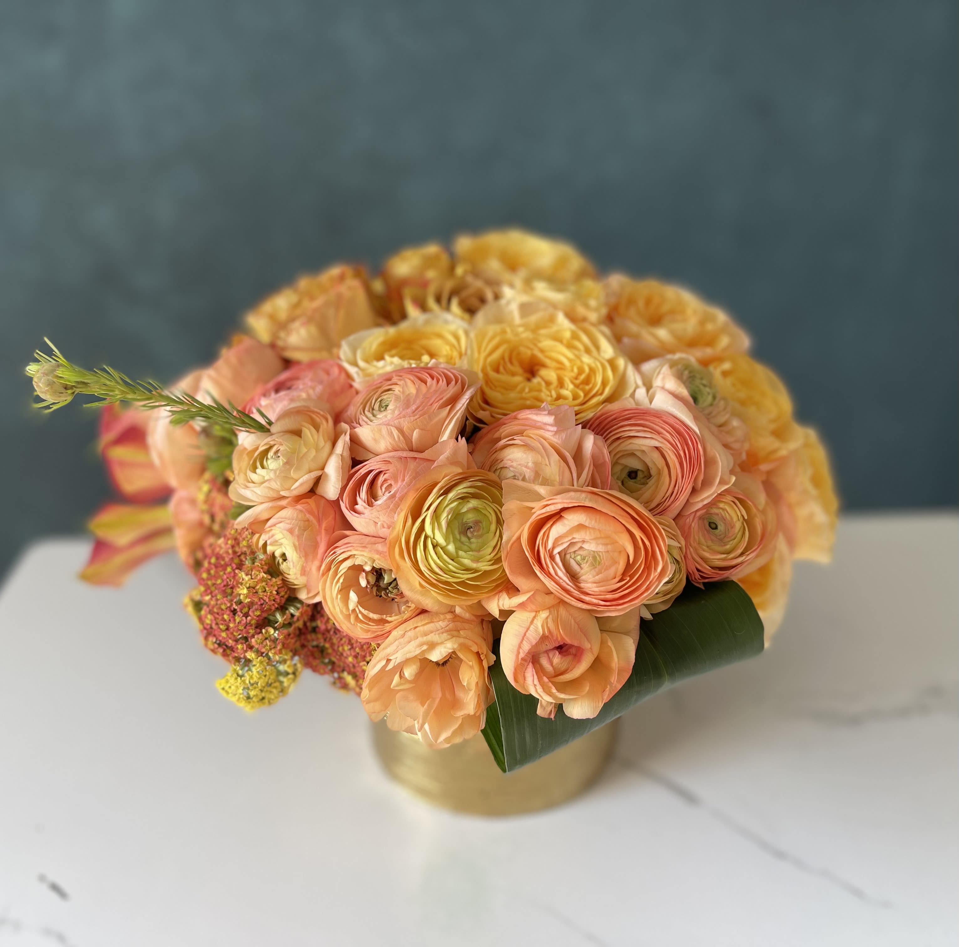 Round bouquet of peach and yellow flowers in a gold vase