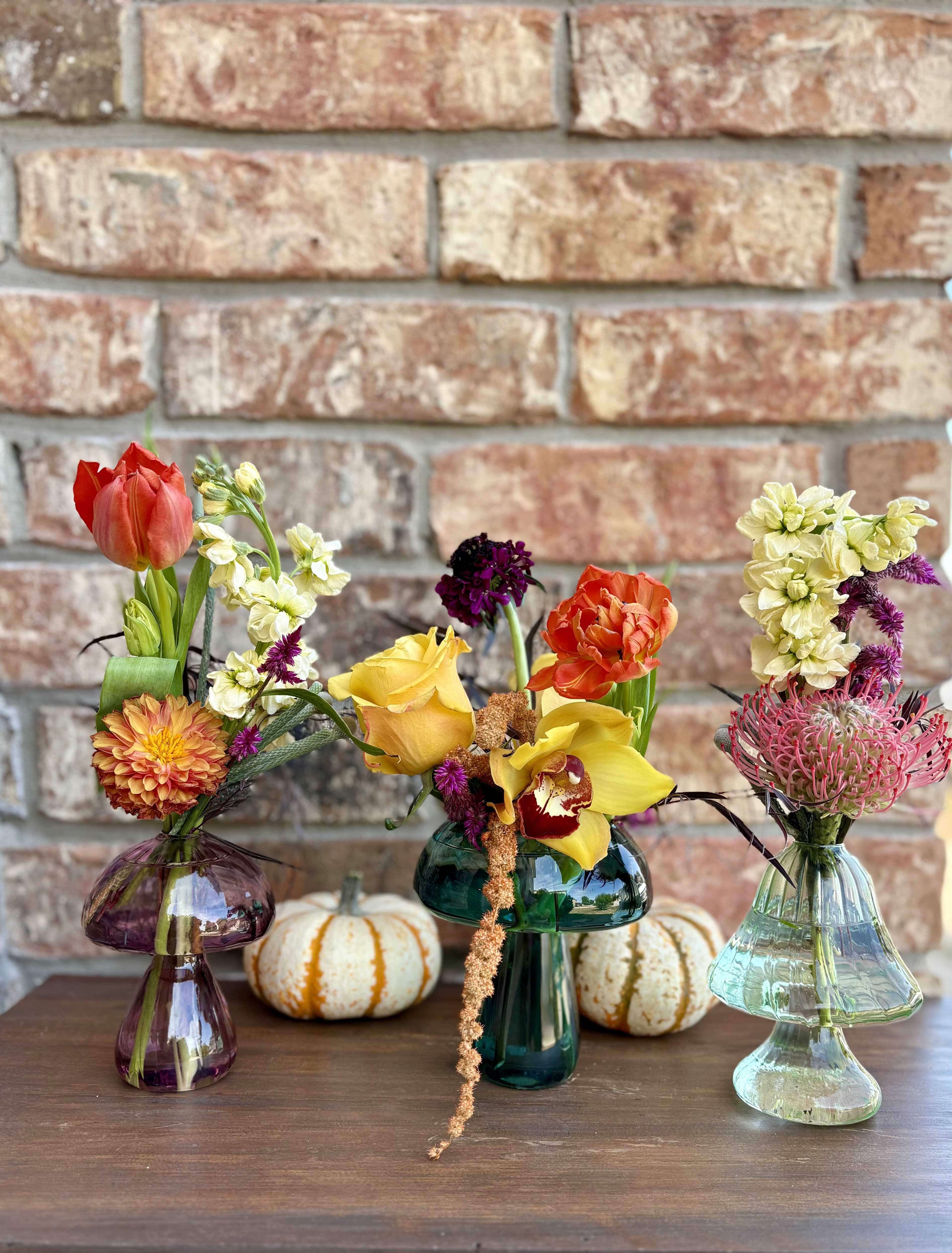 Meadow Shroom Collection - A whimsical gathering of mushroom-shaped bud vases, each brimming with unique seasonal blooms. From fiery pincushions and elegant cymbidium orchids to playful tulips, dahlias, roses, and textural accents like amaranthus, celosia, and brunia—this set is designed to groove across your table or scatter throughout your home. Whether clustered together as a funky centerpiece or sprinkled around for little pops of floral magic, the Meadow Shroom Collection brings a retro-boho vibe to any space