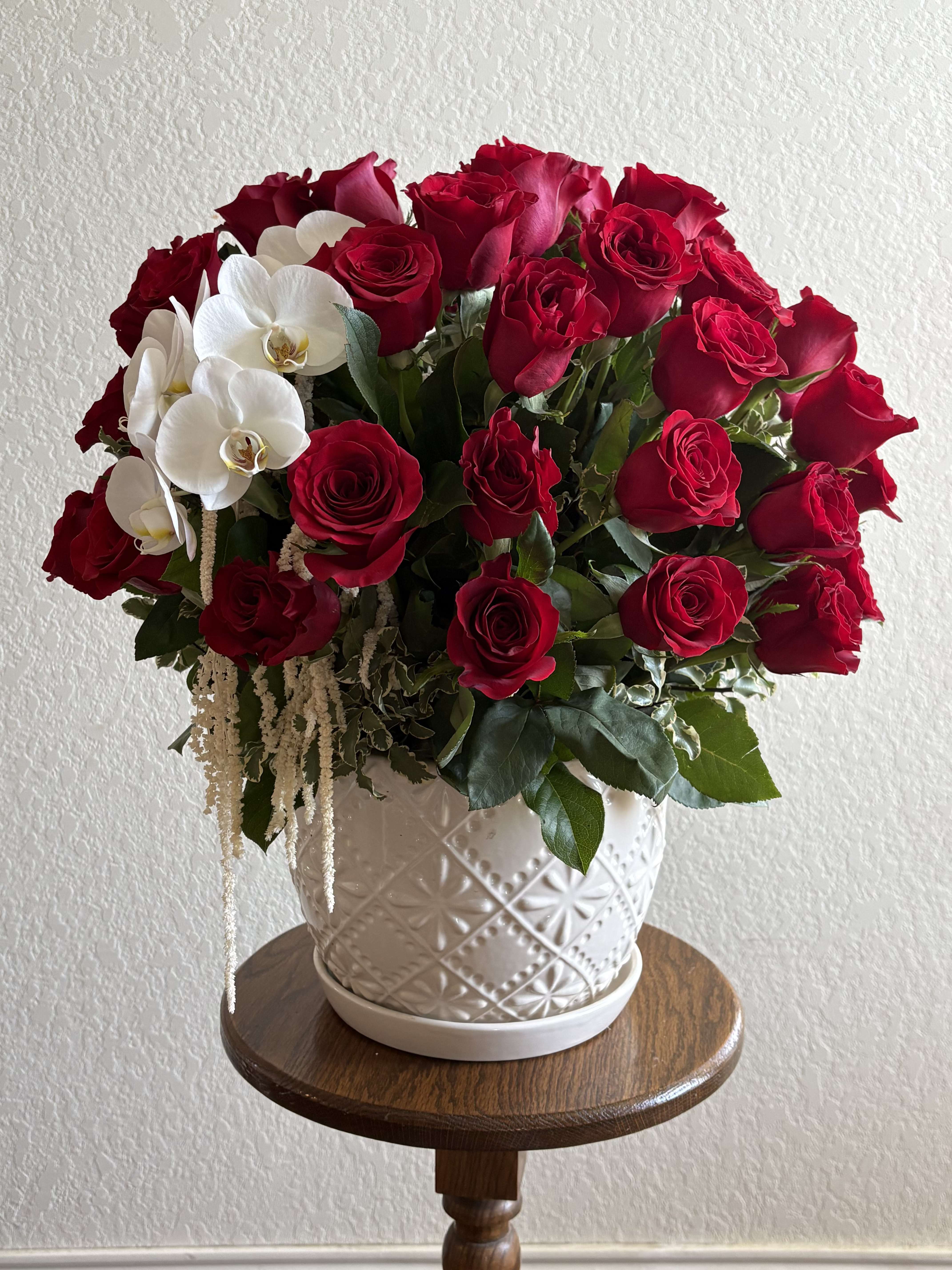 Red roses and white orchids arranged in a white ceramic vase