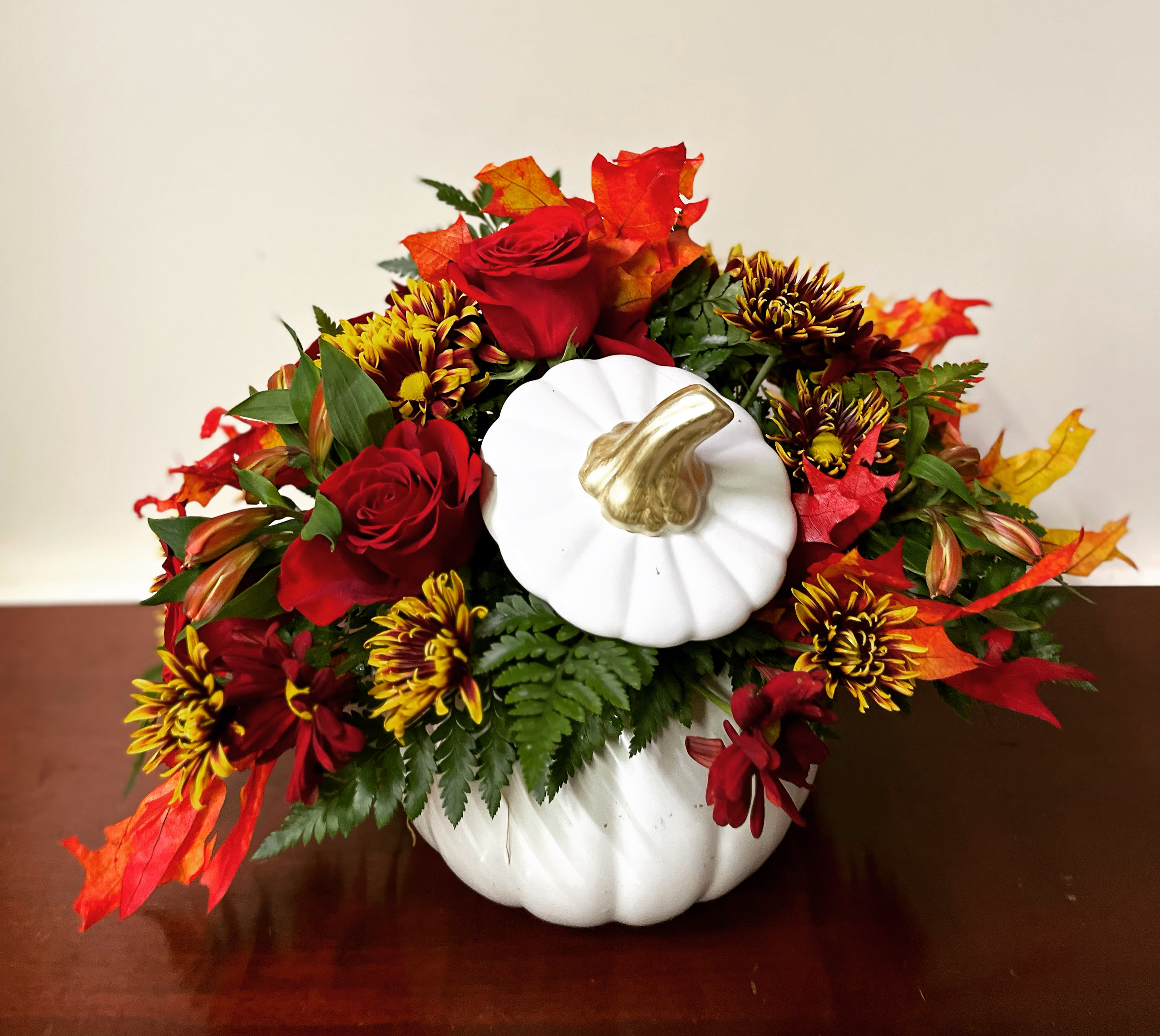 Fall floral arrangement in a white pumpkin container with red roses and mums