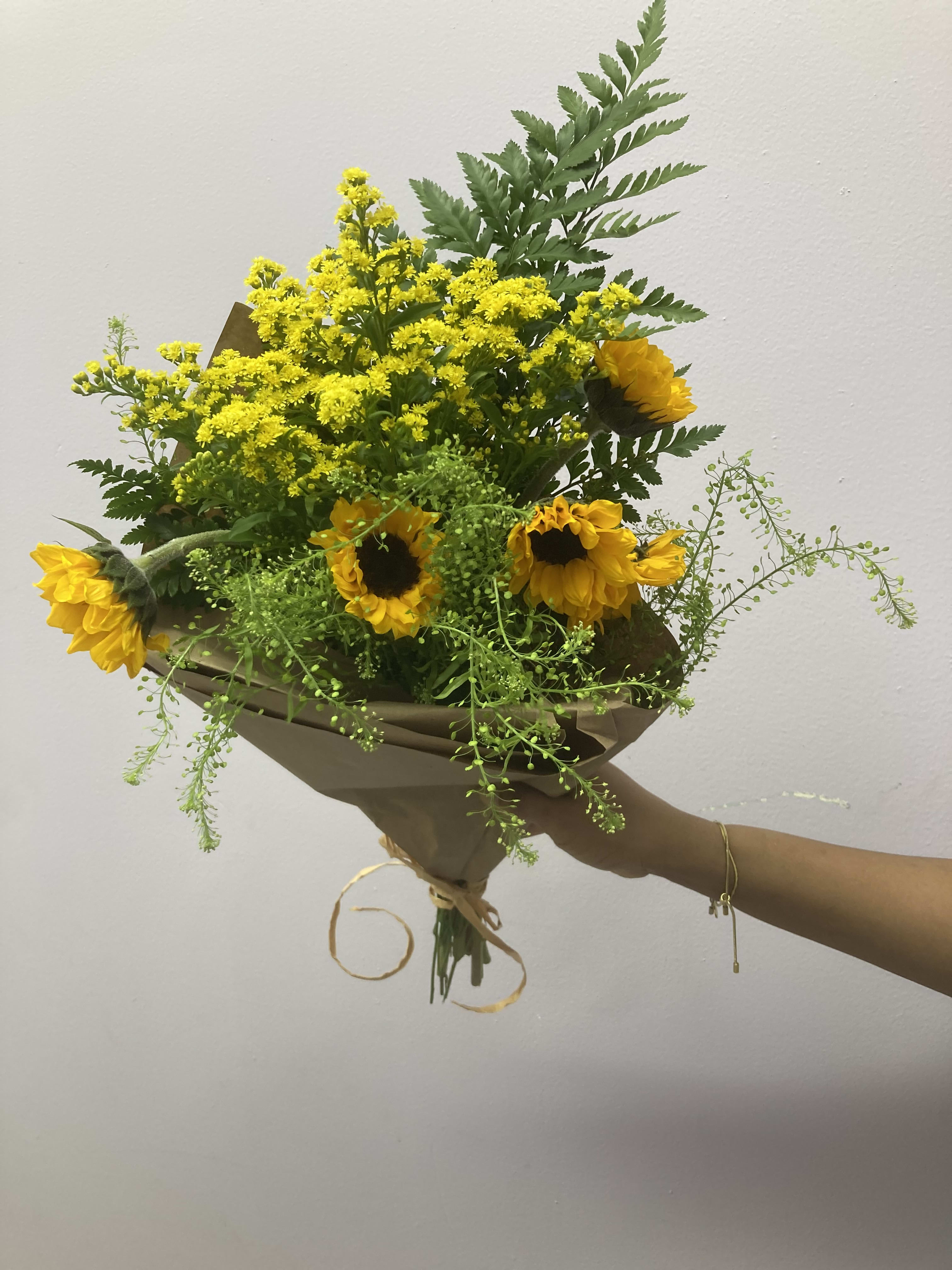 Bouquet of yellow sunflowers and small yellow filler flowers wrapped in brown paper