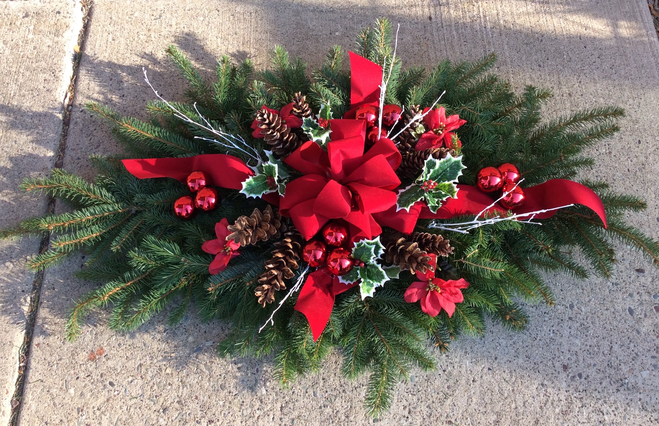 Grave Blanket - Honor your loved ones with a hand-crafted grave blanket from Blue Violet Flower Studio. Each blanket is thoughtfully designed with a lush mix of fresh evergreens, pinecones, bows, and seasonal accents—symbolizing warmth, remembrance, and eternal peace.  Available in a variety of sizes and styles, our grave blankets are made with care to withstand winter weather and bring lasting beauty to the resting place throughout the holiday season. Custom ribbon colors, flowers, and personalization options are available upon request.  We offer local delivery to cemeteries in Warrington, PA and surrounding Bucks County areas, or you may schedule a convenient in-store pickup.  To place an order or discuss special requests, please call us at (215) 220-1000.