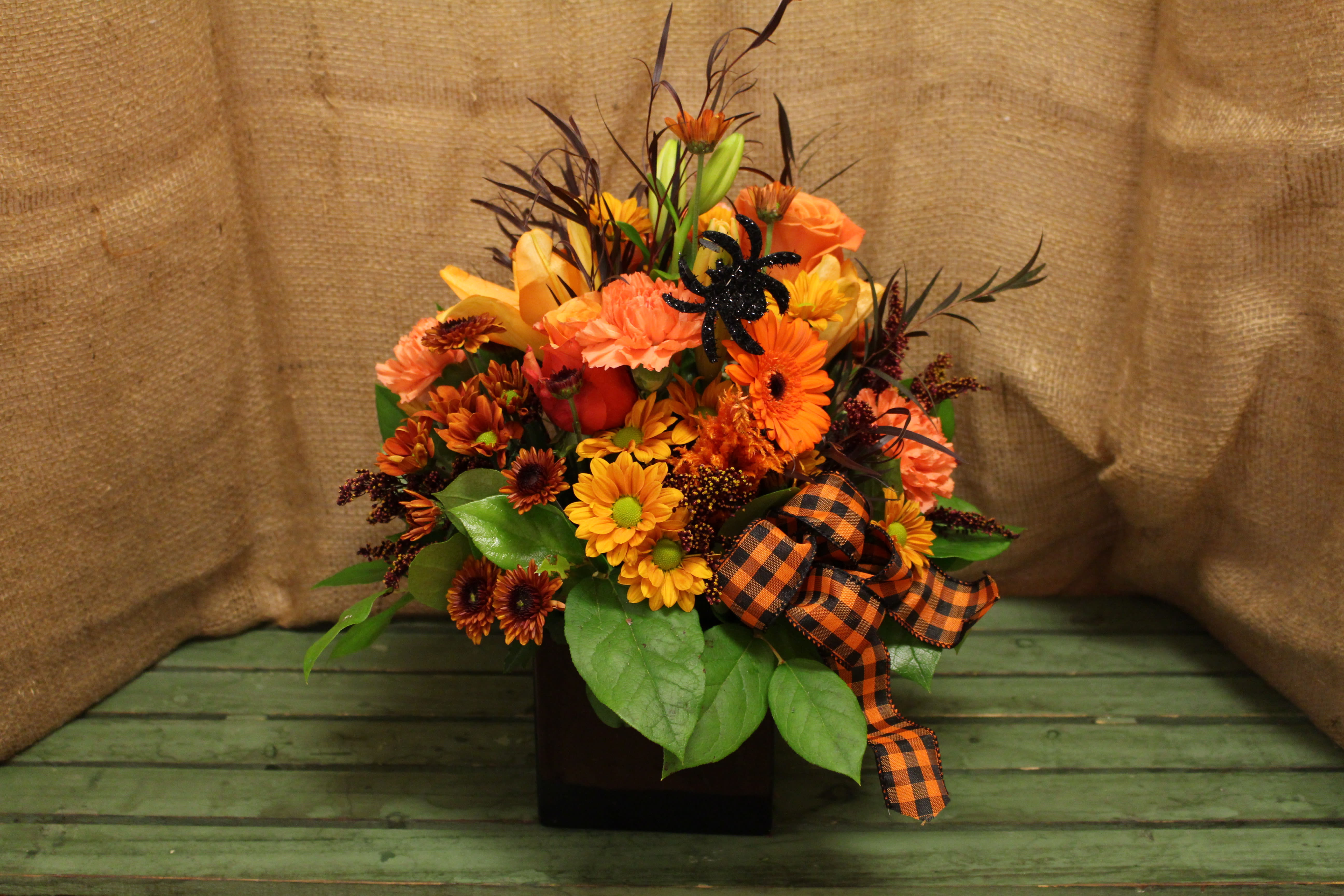 Spooky Central - This black cube is filled to the brim with festive fall flowers, and is the perfect way to celebrate Halloween while maintaining a classic feel. With added touches like a black and orange checked bow and a small decorative spider, this piece is the perfect way to celebrate the holiday in style.