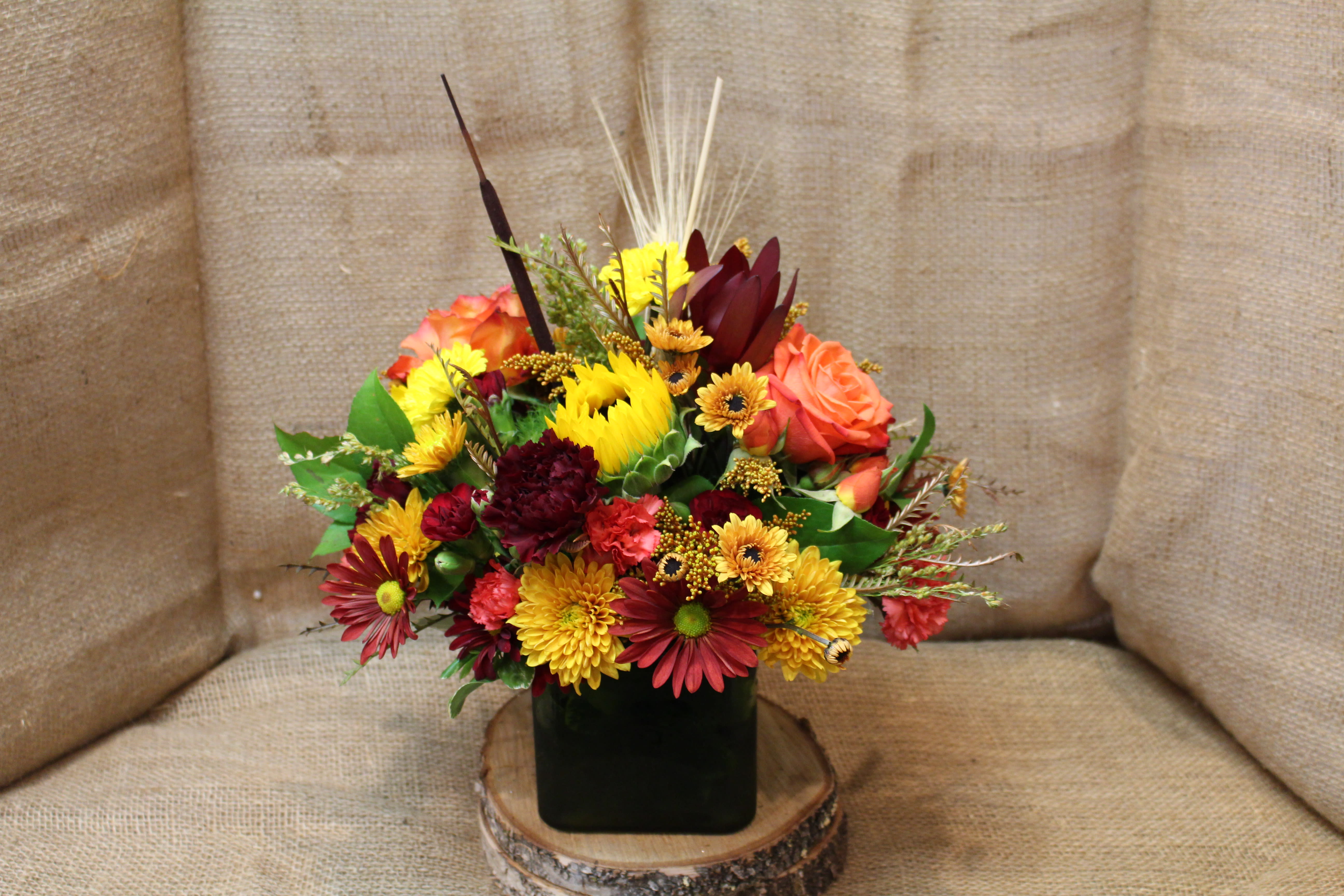 Mixed bouquet of red, orange, and yellow flowers in a dark square vase