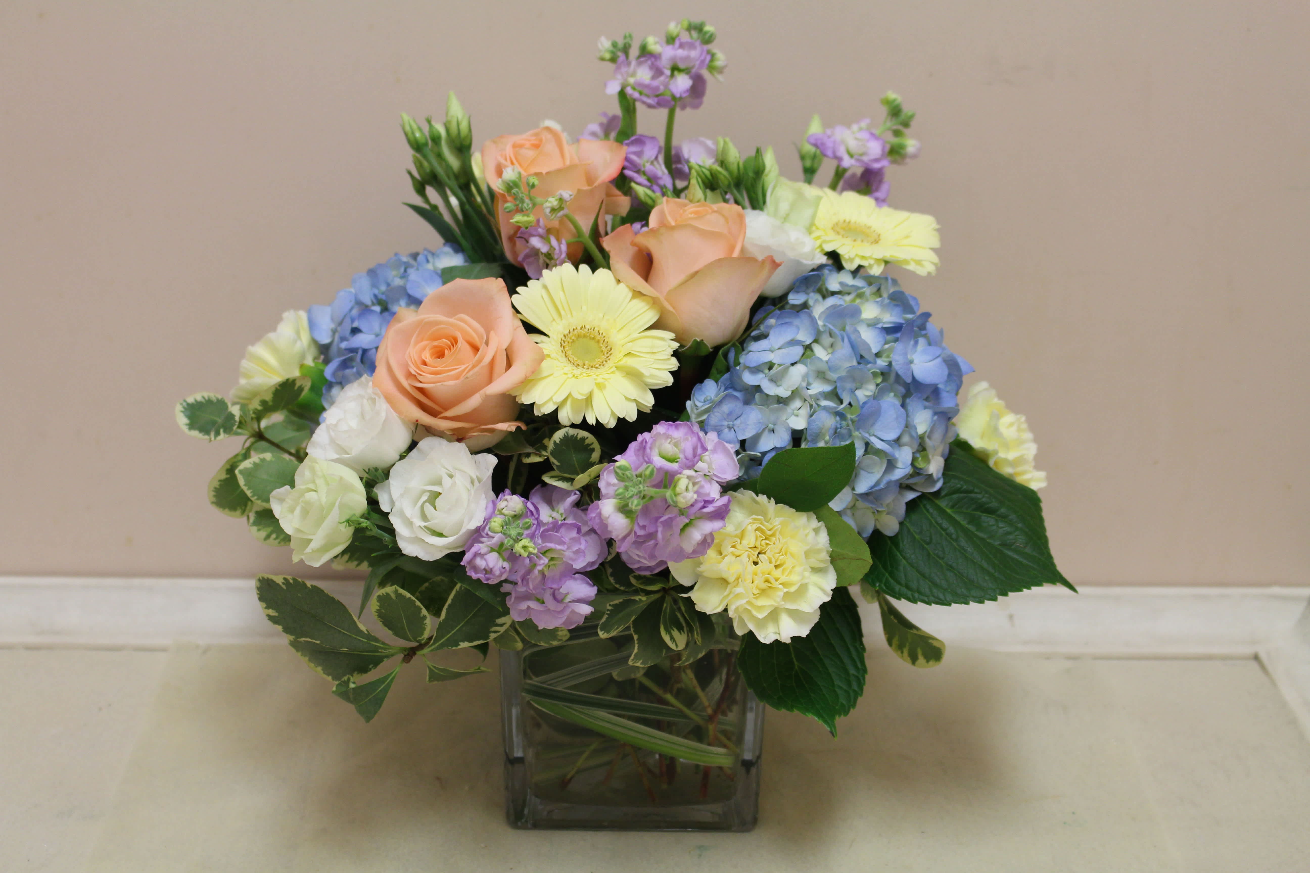Mixed bouquet of roses, hydrangeas, and daisies in a square glass vase