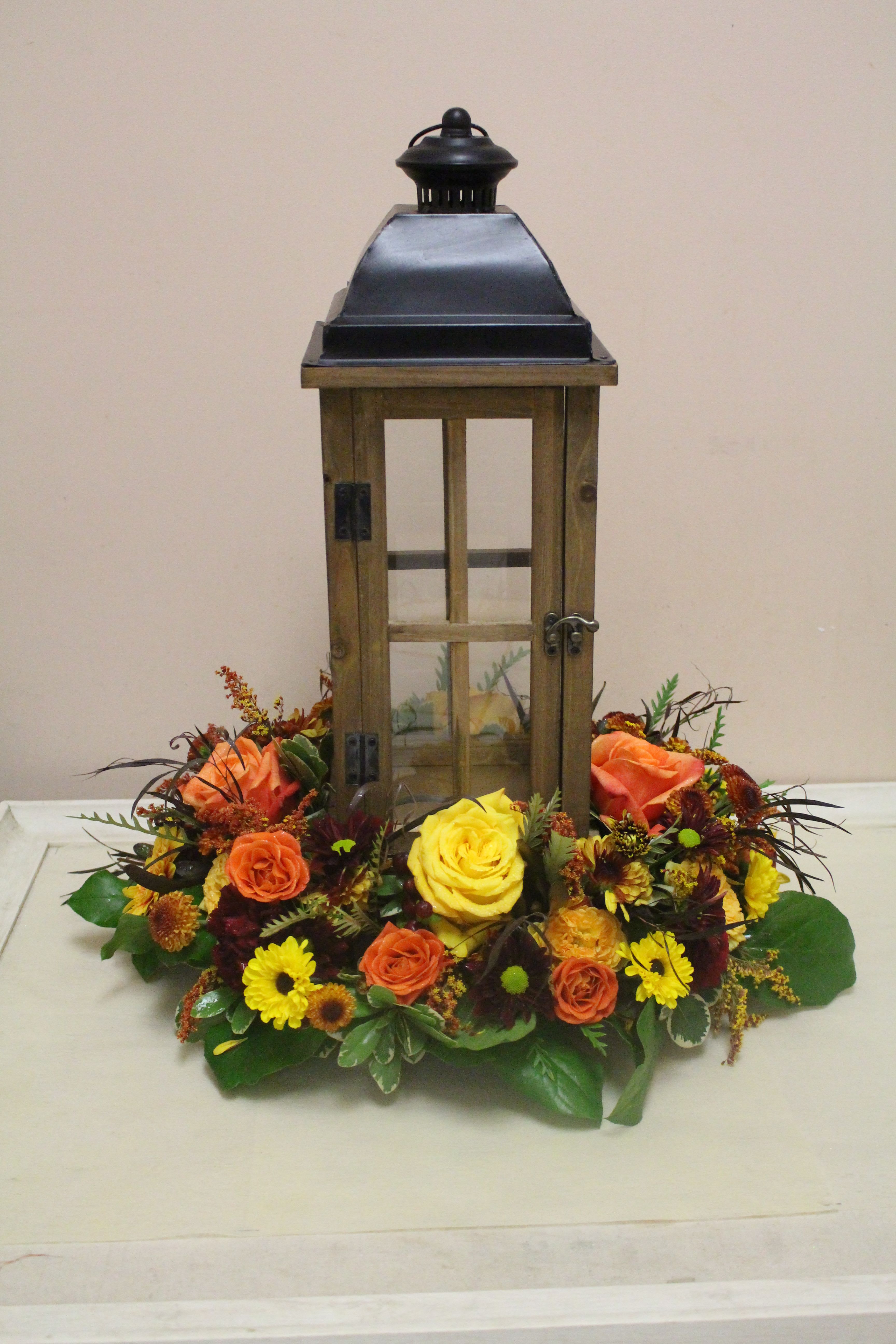 Lantern centerpiece surrounded by orange, yellow, and burgundy flowers