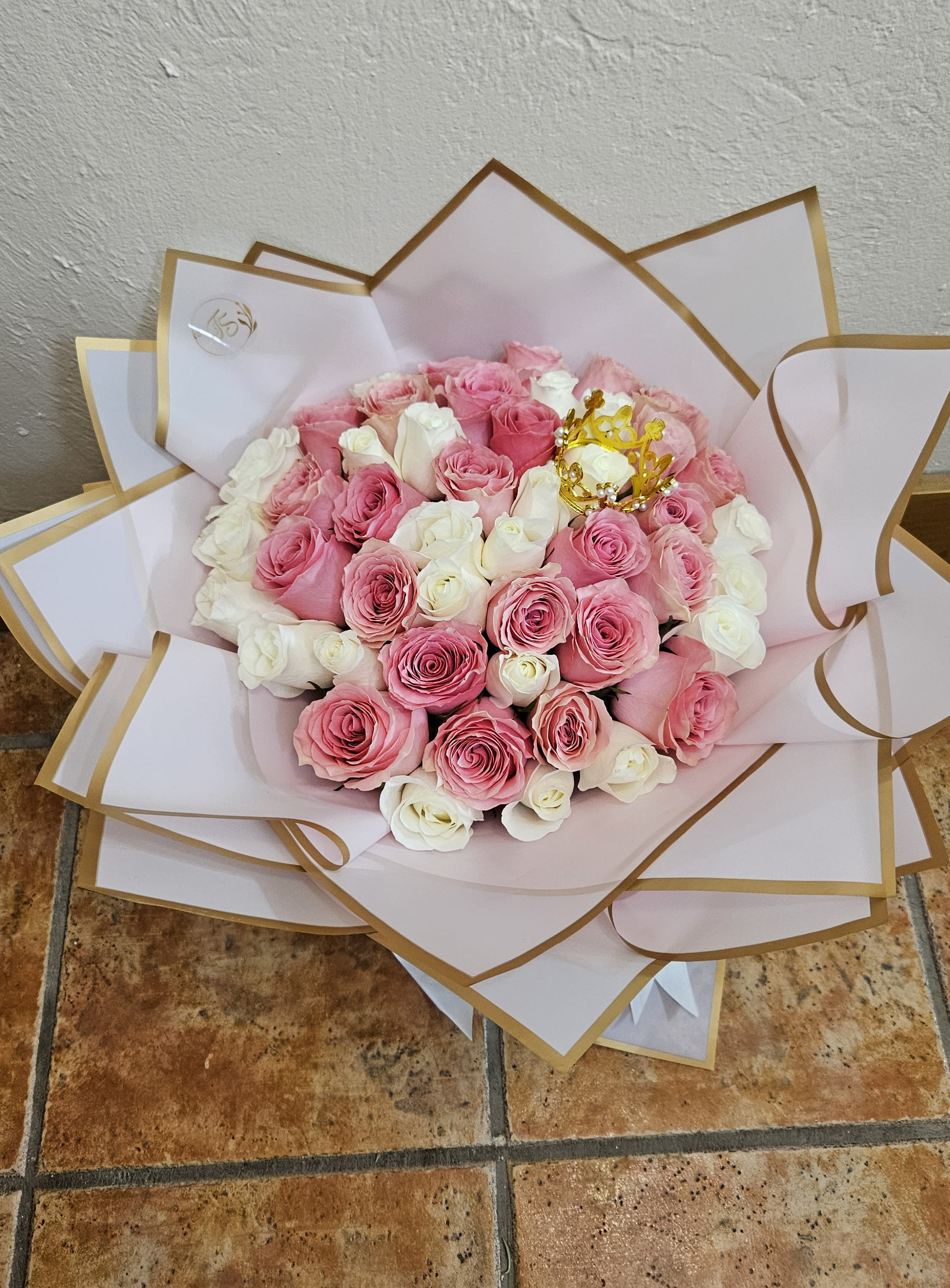 Bouquet of pink and white roses wrapped in white paper with gold trim