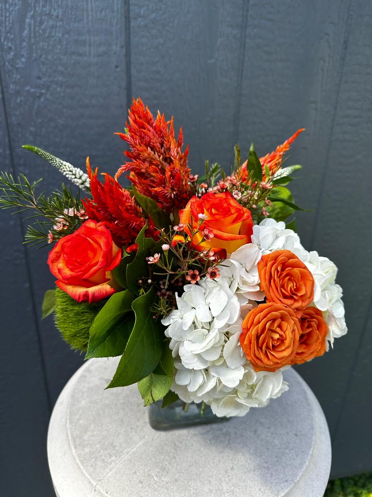 Orange roses and white hydrangeas in a glass vase with red plumes