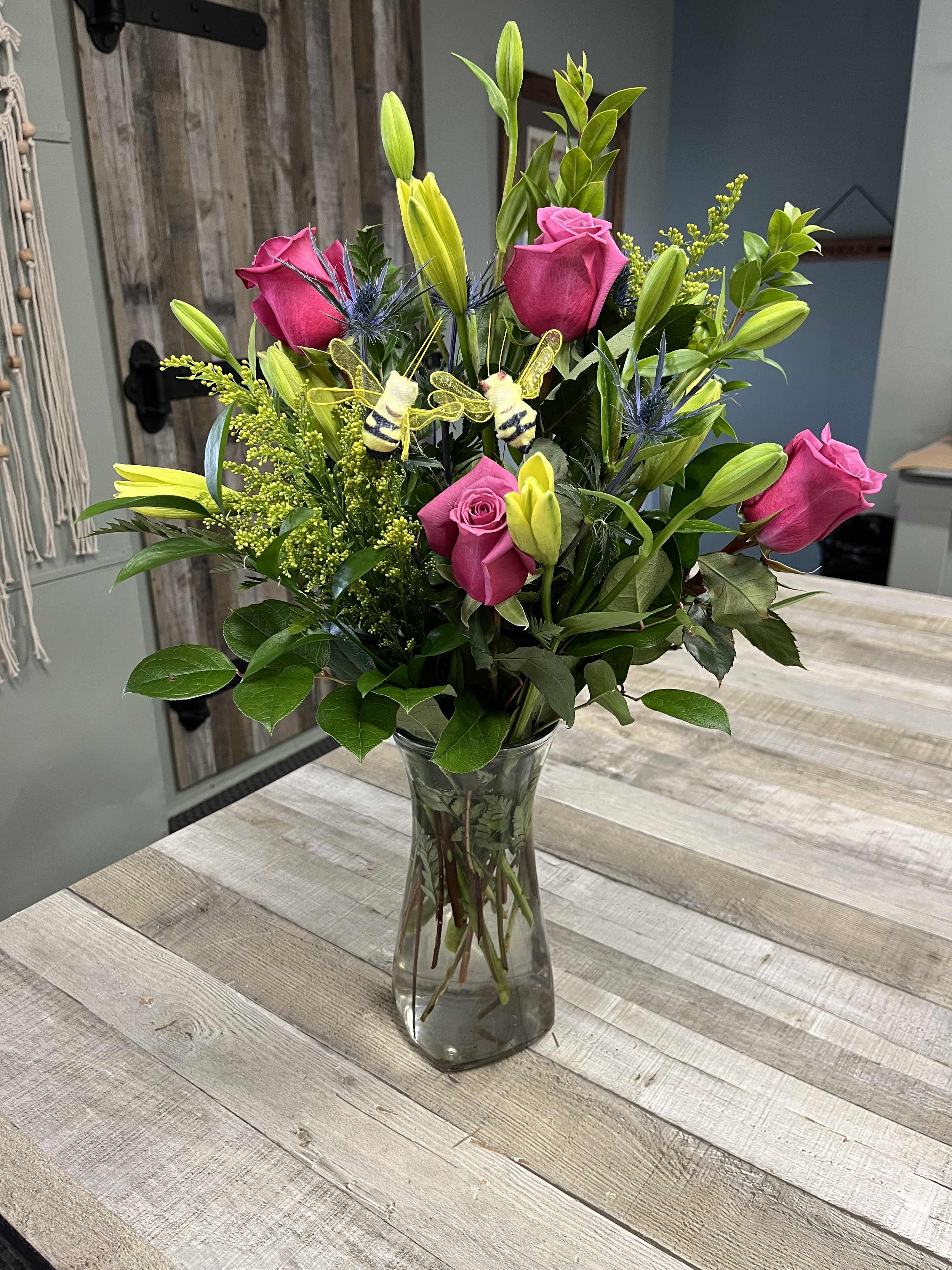 Pink roses and yellow lilies in a clear glass vase with bee decorations